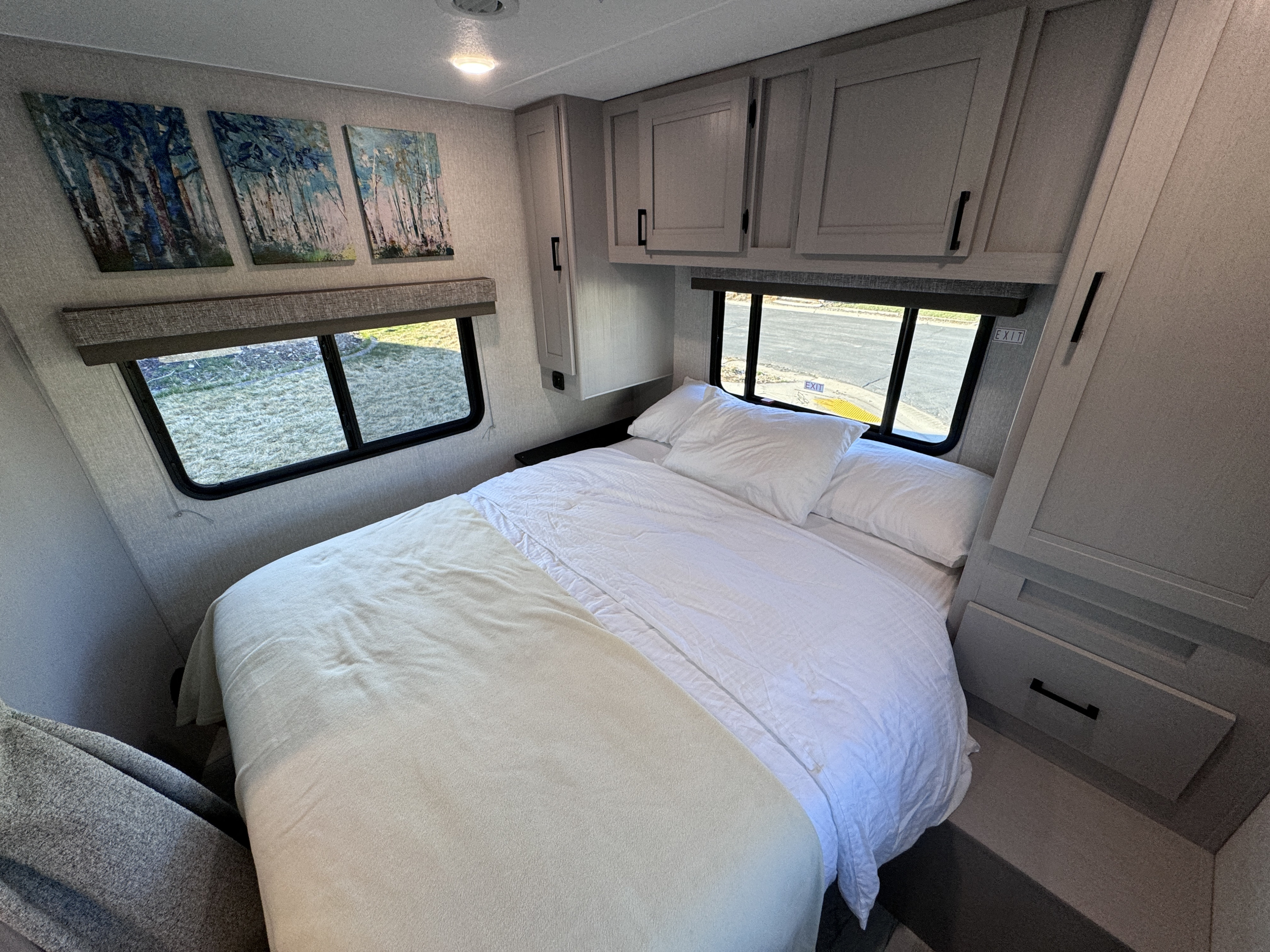 Modern RV rental bedroom featuring a comfortable bed, wall art, overhead storage, and windows with an outdoor view.. Forest River Coachmen Freelander 2025
