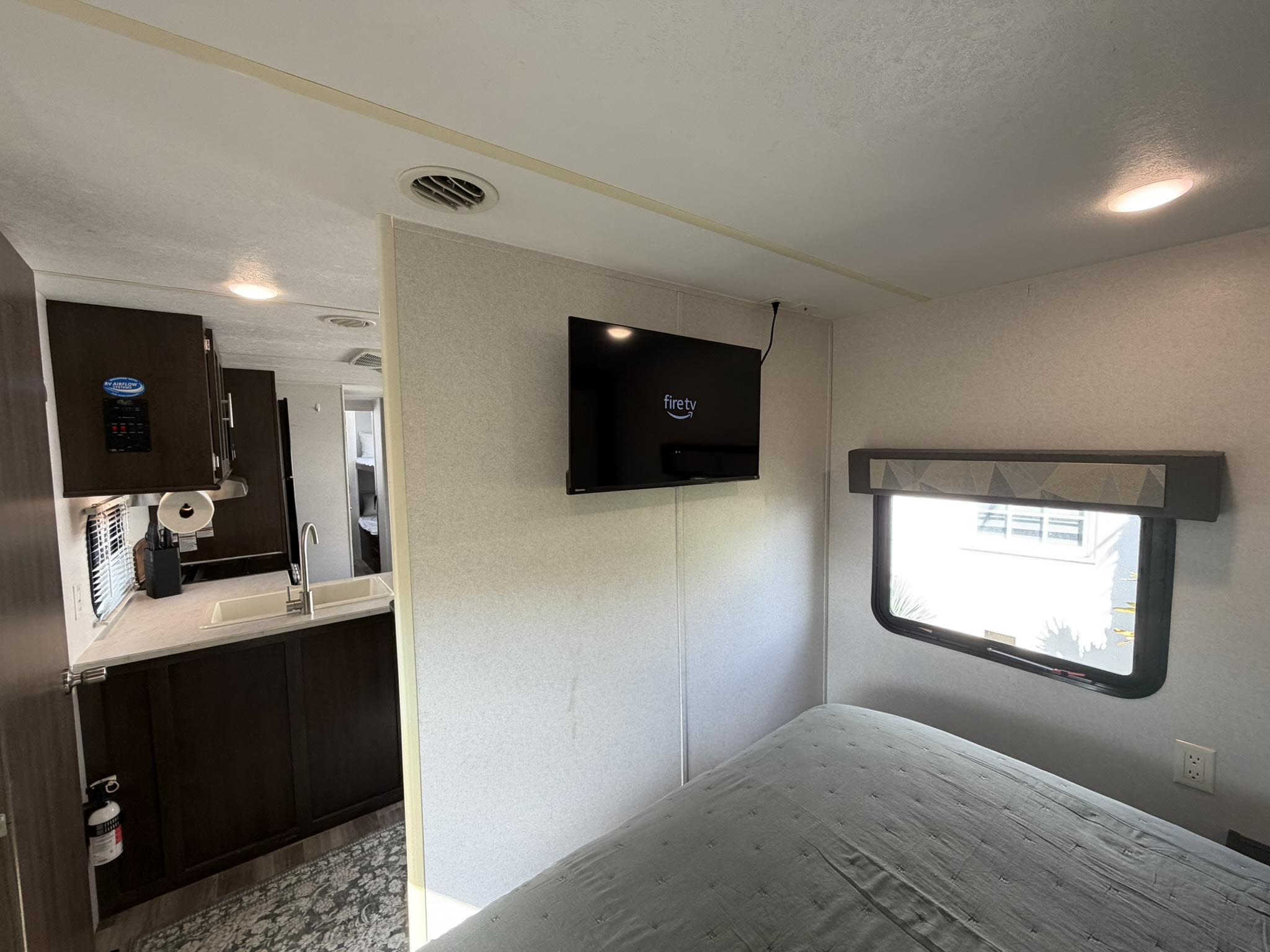 RV rental interior: a compact kitchen on the left, a cozy bedroom with a flat-screen TV and window on the right.. Forest River Wildwood 2020