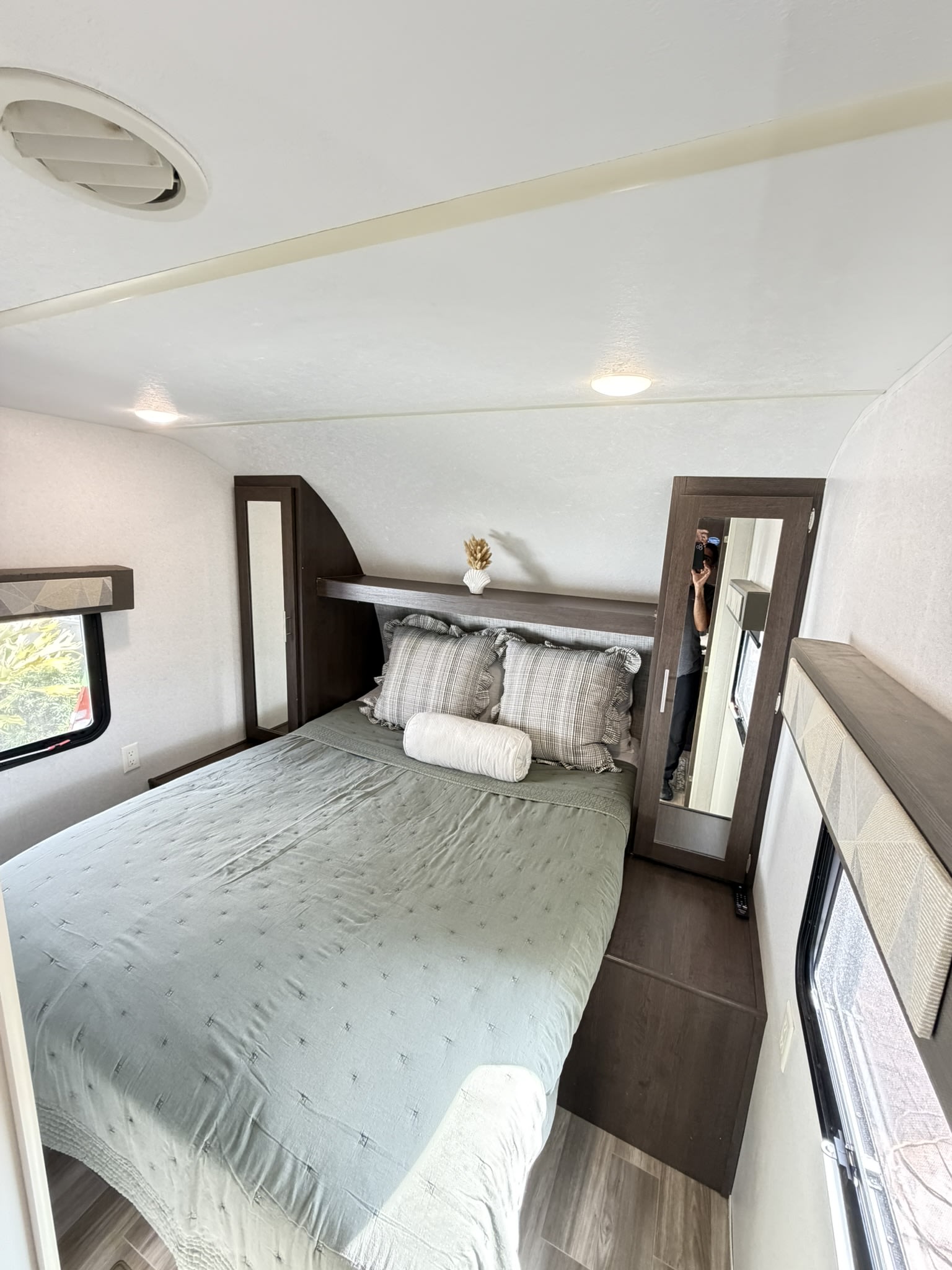 Cozy RV rental bedroom featuring a bed with sage bedding, mirrored wardrobe, windows, and overhead lighting.. Forest River Wildwood 2020