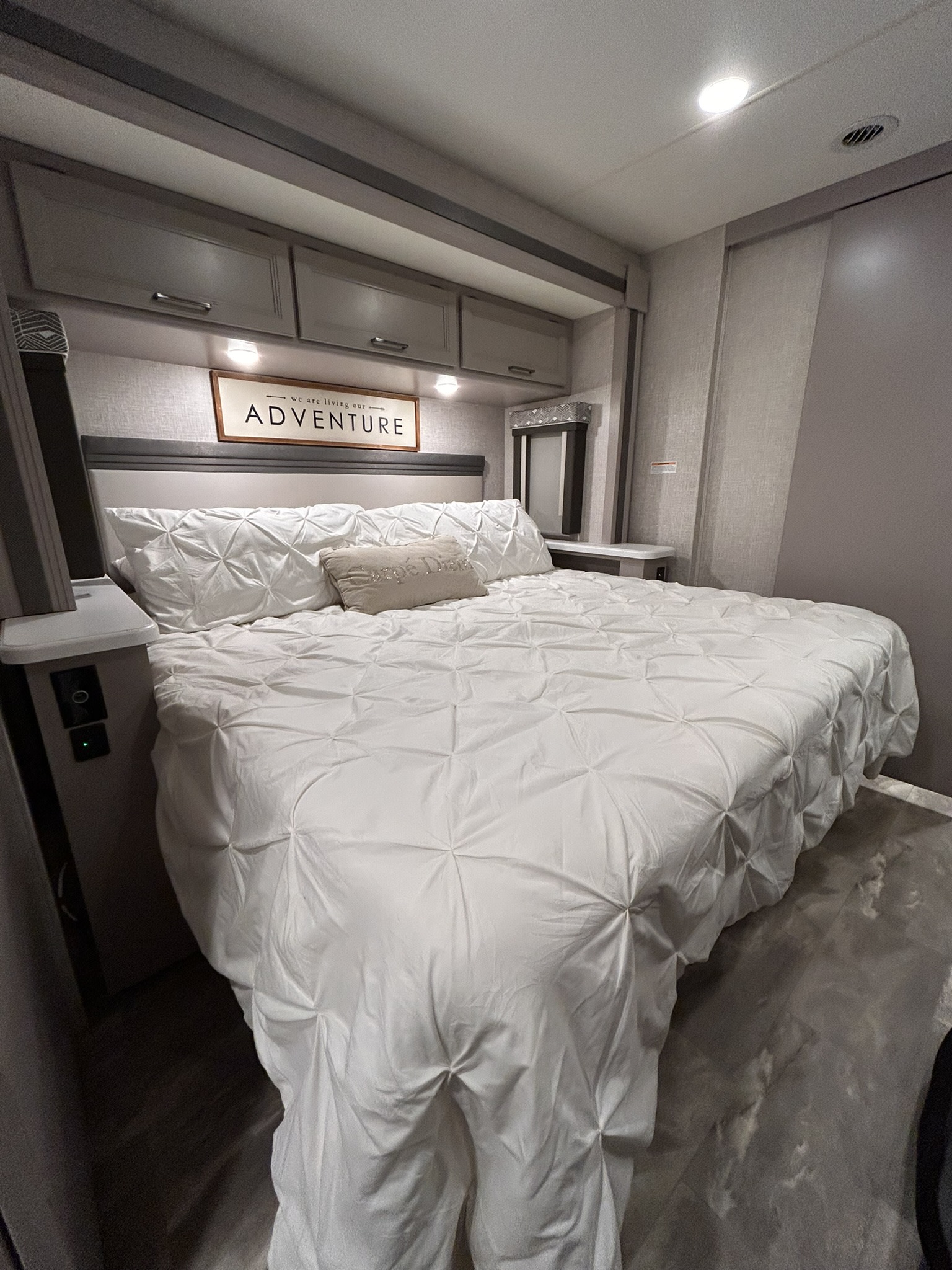 Cozy RV rental bedroom with modern design, white pintuck bedding, and an 'ADVENTURE' sign above the bed. Ready for travel!. Thor Windsport 2023