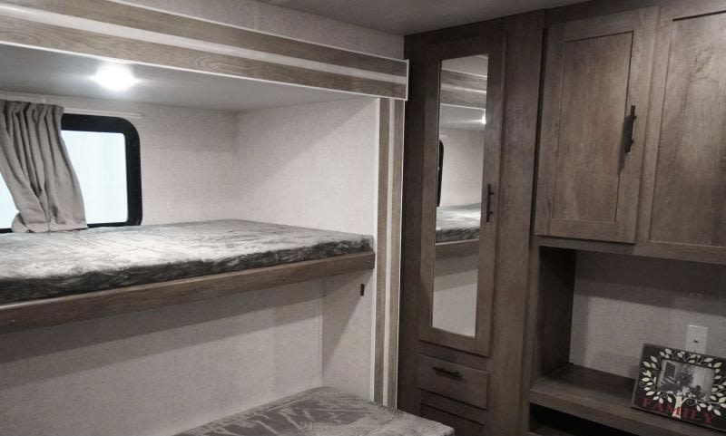 Cozy rv rental bunk bed area with window, curtain, and nearby storage cabinet with a mirror, perfect for family adventures.. Forest River Wildwood 2021