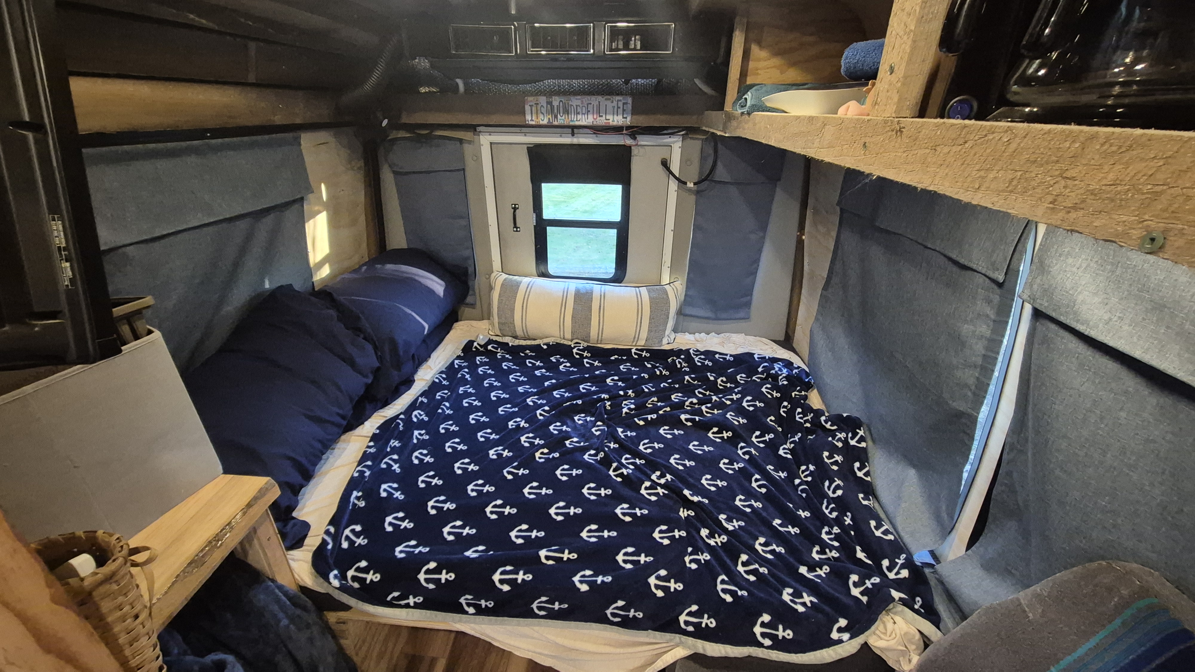 Cozy rv rental camper interior with a bed, nautical anchor blanket, window view, and overhead storage.. Ford E350 Box Van 2005