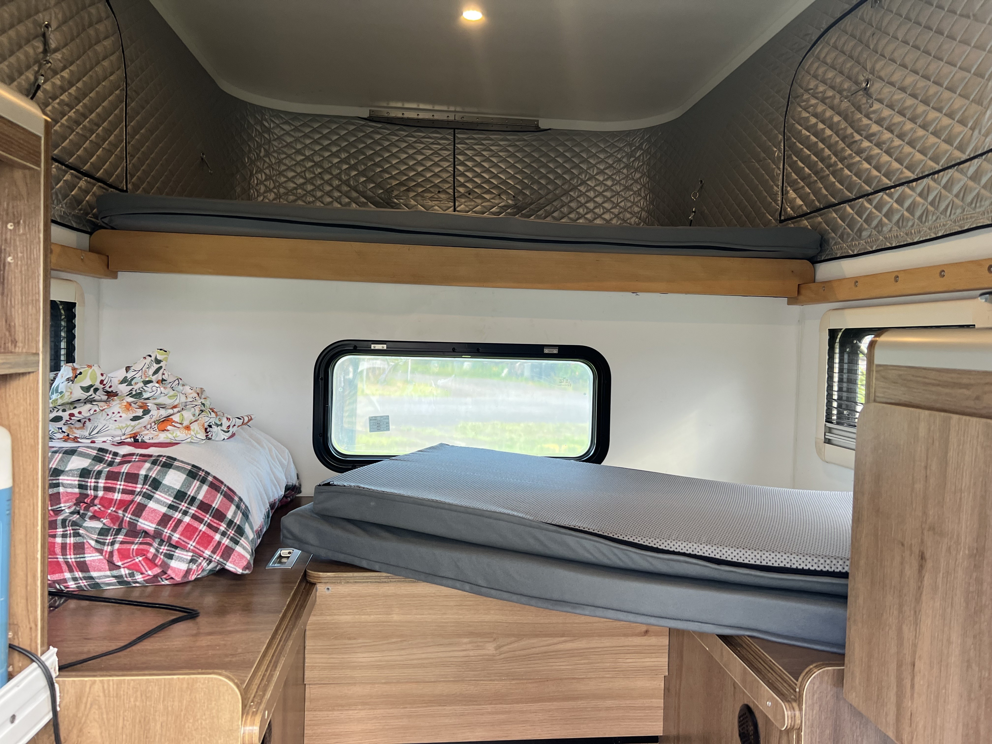 Cozy rv rental interior showing a lower bed with blankets and an upper bunk bed with mattresses, plus multiple windows.. toyota trd 4x4 sport 2017