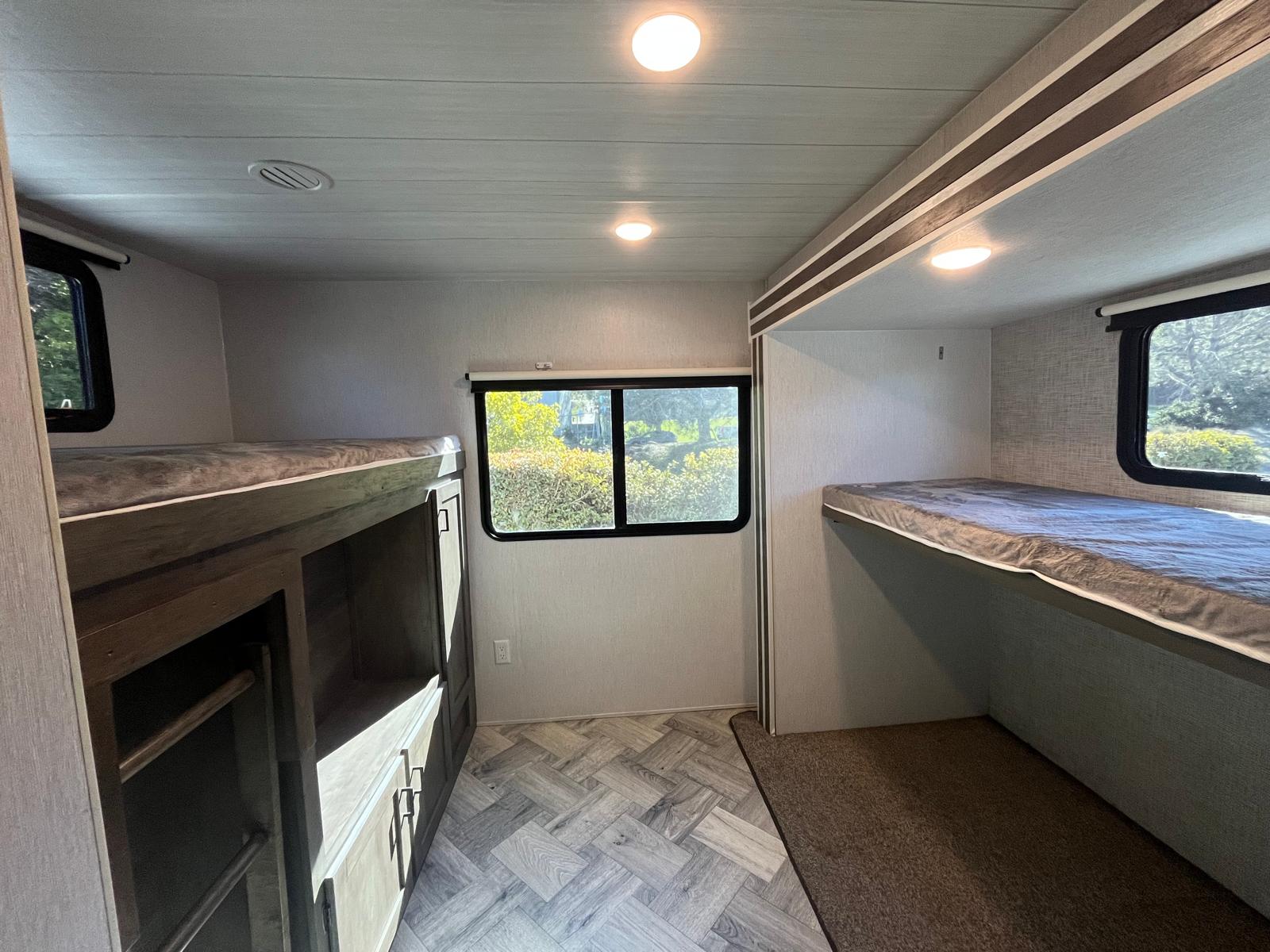 Inside an RV rental bunkhouse: two cozy bunk beds, a window with outdoor views, and built-in storage.. Forest River EVO T3250 2022