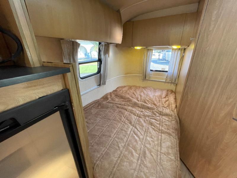 Inside this cozy **RV rental**: a bed, two windows with curtains, overhead storage, and a small fridge on the left.. Airstream Safari 2004