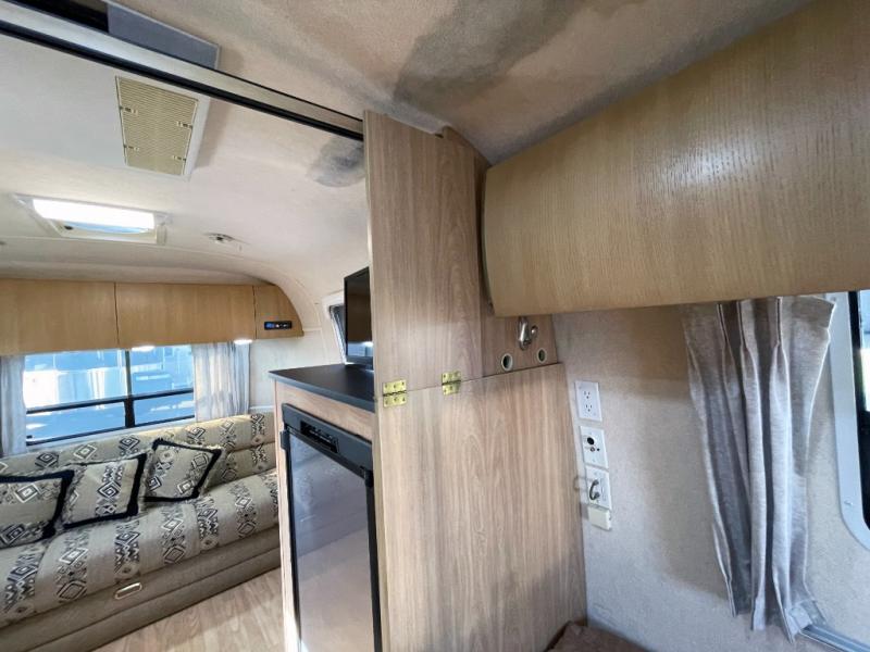 Inside this rv rental, a light wood interior reveals a sofa, small fridge, TV, and overhead storage, defining a cozy living space.. Airstream Safari 2004