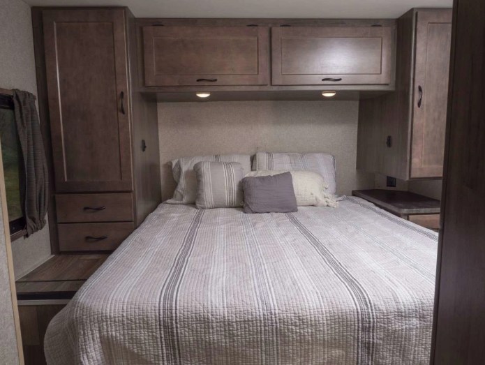 Cozy RV rental bedroom with a comfortable bed, striped quilt, overhead cabinets, and side storage.. Winnebago Minnie Winnie 2020