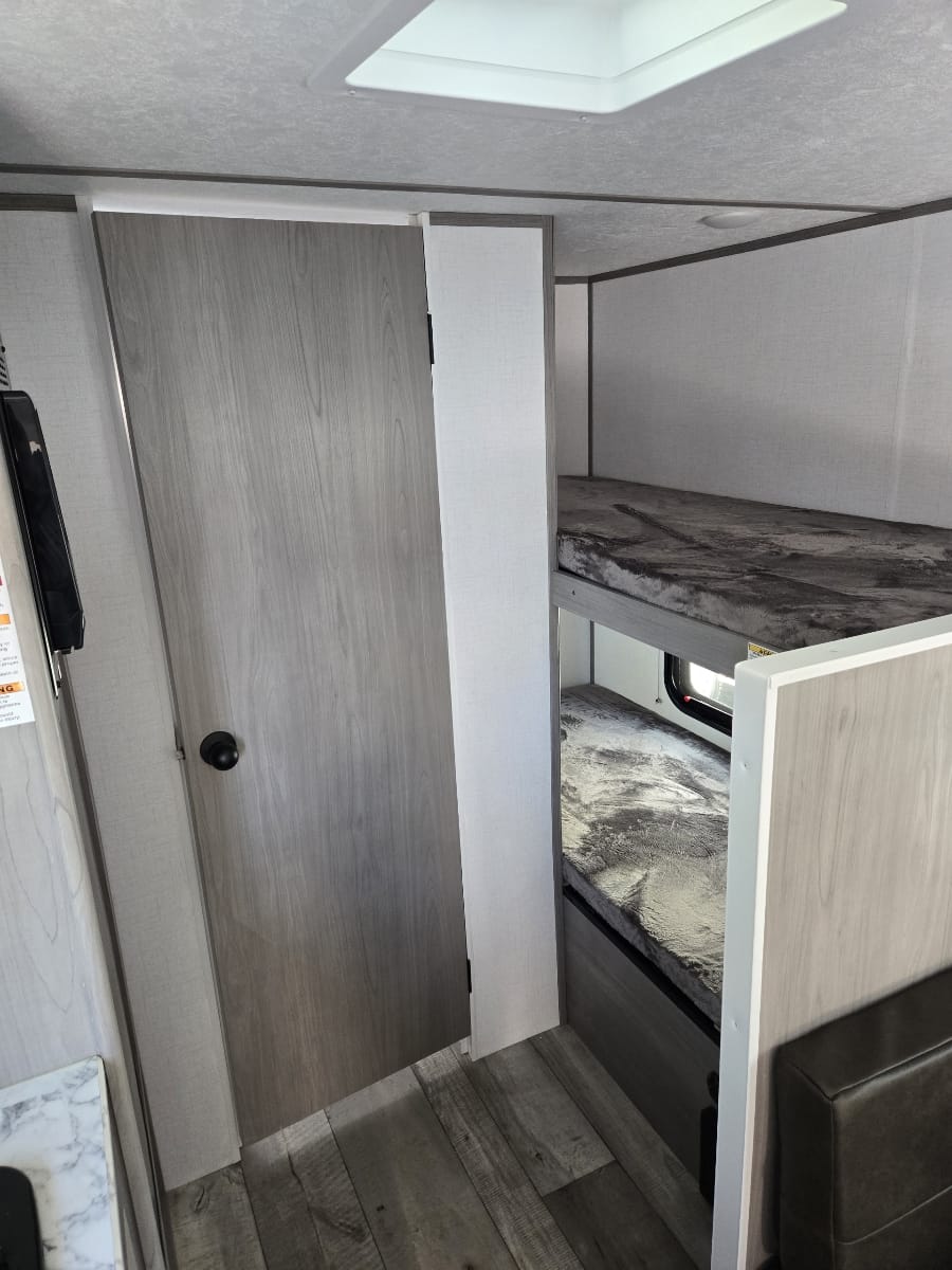 Cozy rv rental interior with bunk beds, a light wood door, skylight, and vinyl plank flooring.. Dutchmen Coleman 2024