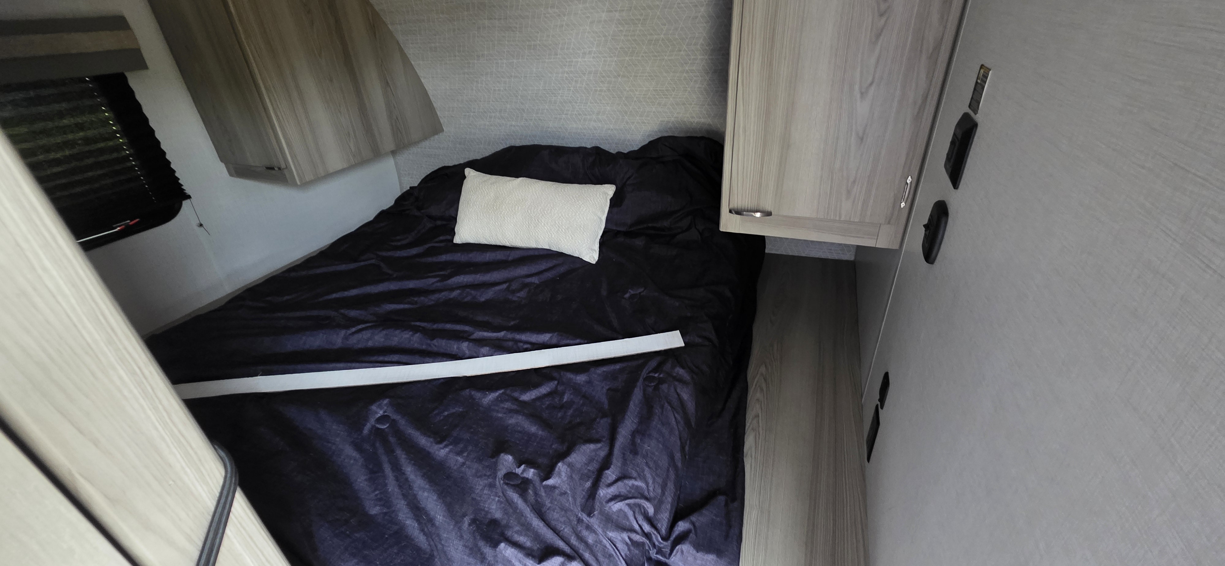 RV rental bedroom showing dark bed with pillow, light wood cabinets, and a window with dark blinds.. Forest River Wildwood FSX Platinum 2024