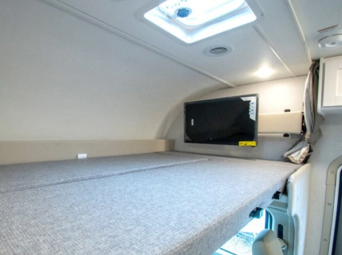 This RV rental features a spacious bunk over the cab with a comfortable gray mattress, a mounted TV, and an overhead skylight.. Thor Motor Coach Four Winds 2026
