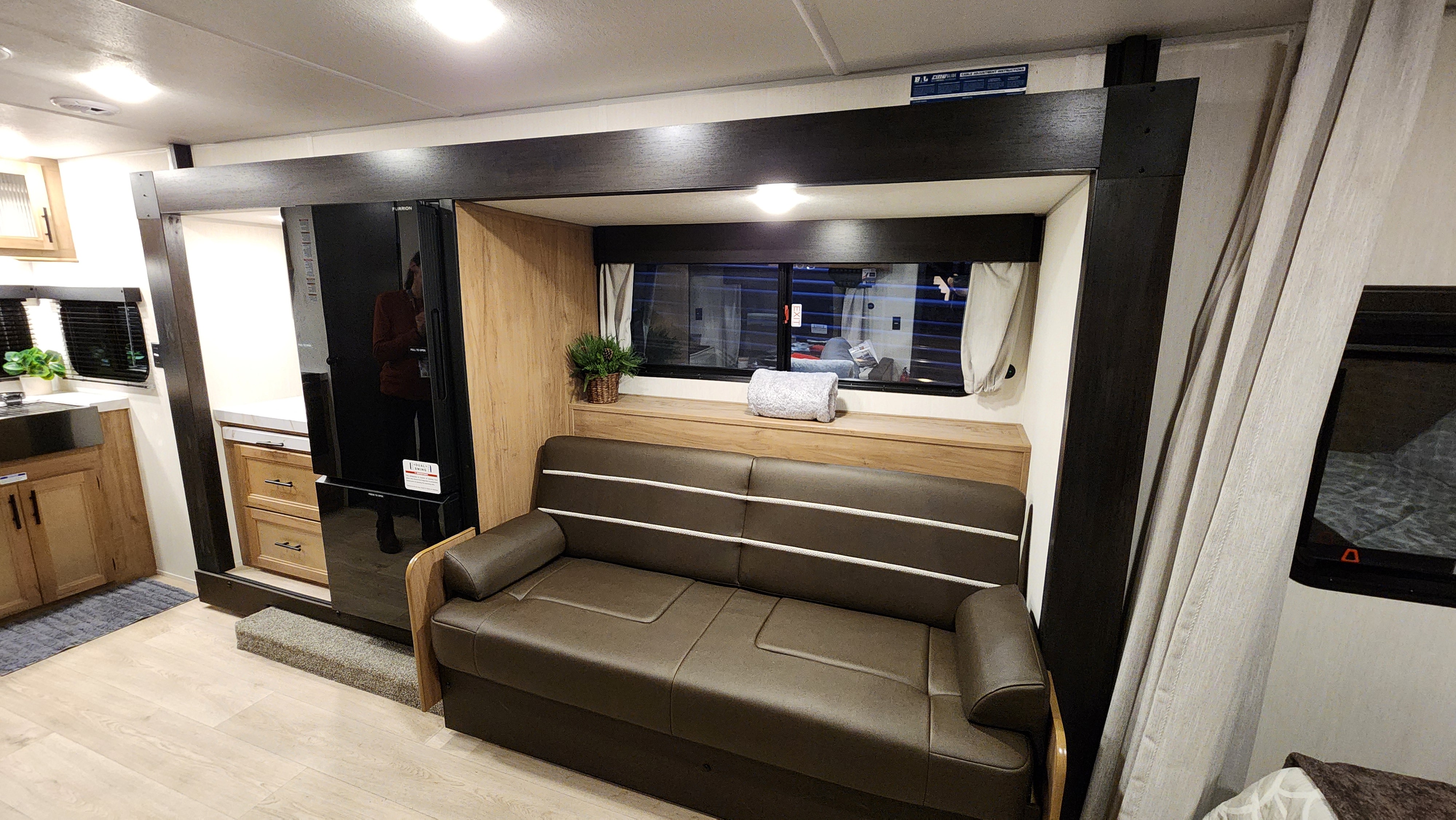 An RV rental interior featuring a brown sofa, a dark refrigerator, and a kitchen area, all within a compact, modern design.. Forest River Cherokee Grey Wolf 2025