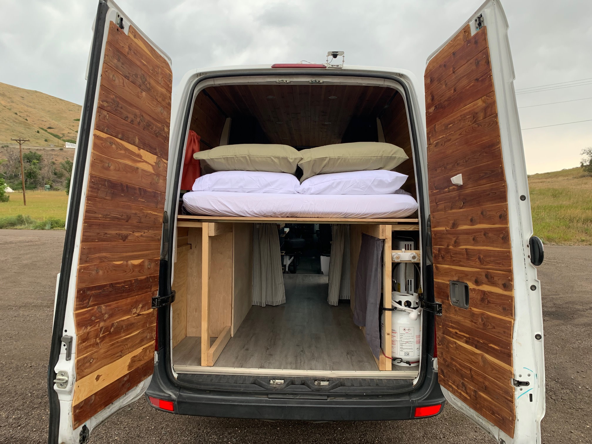 Cozy **rv rental** van conversion interior, revealing a bed, wooden paneling, storage, and a propane tank setup.. Mercedes Sprinter 2011