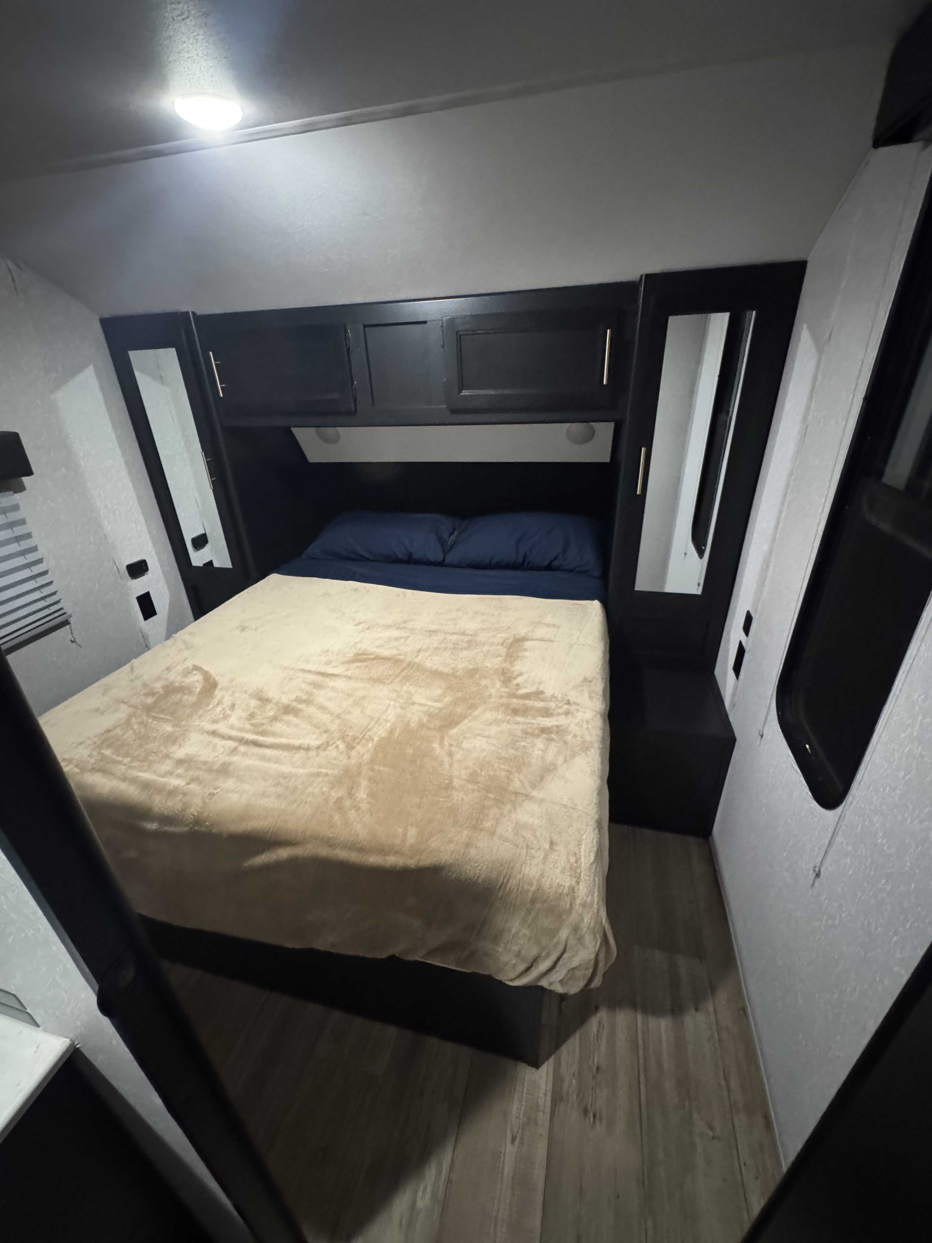 Cozy RV rental bedroom with a bed, dark cabinetry, mirrors, light walls, and wood-look floor.. Forest River Cherokee Grey Wolf 2022