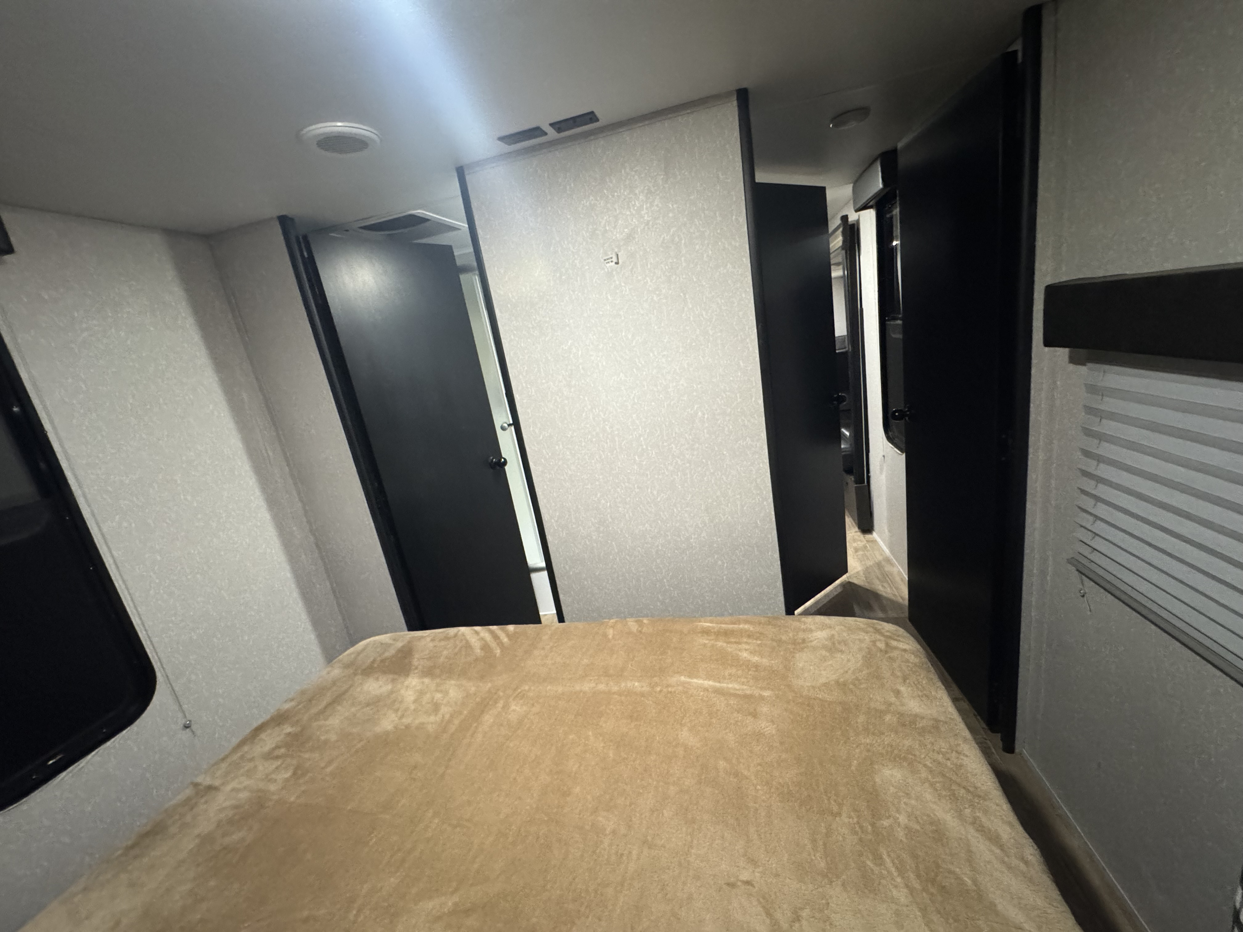 This RV rental features a compact bedroom area with a bed, light walls, and multiple dark doors.. Forest River Cherokee Grey Wolf 2022