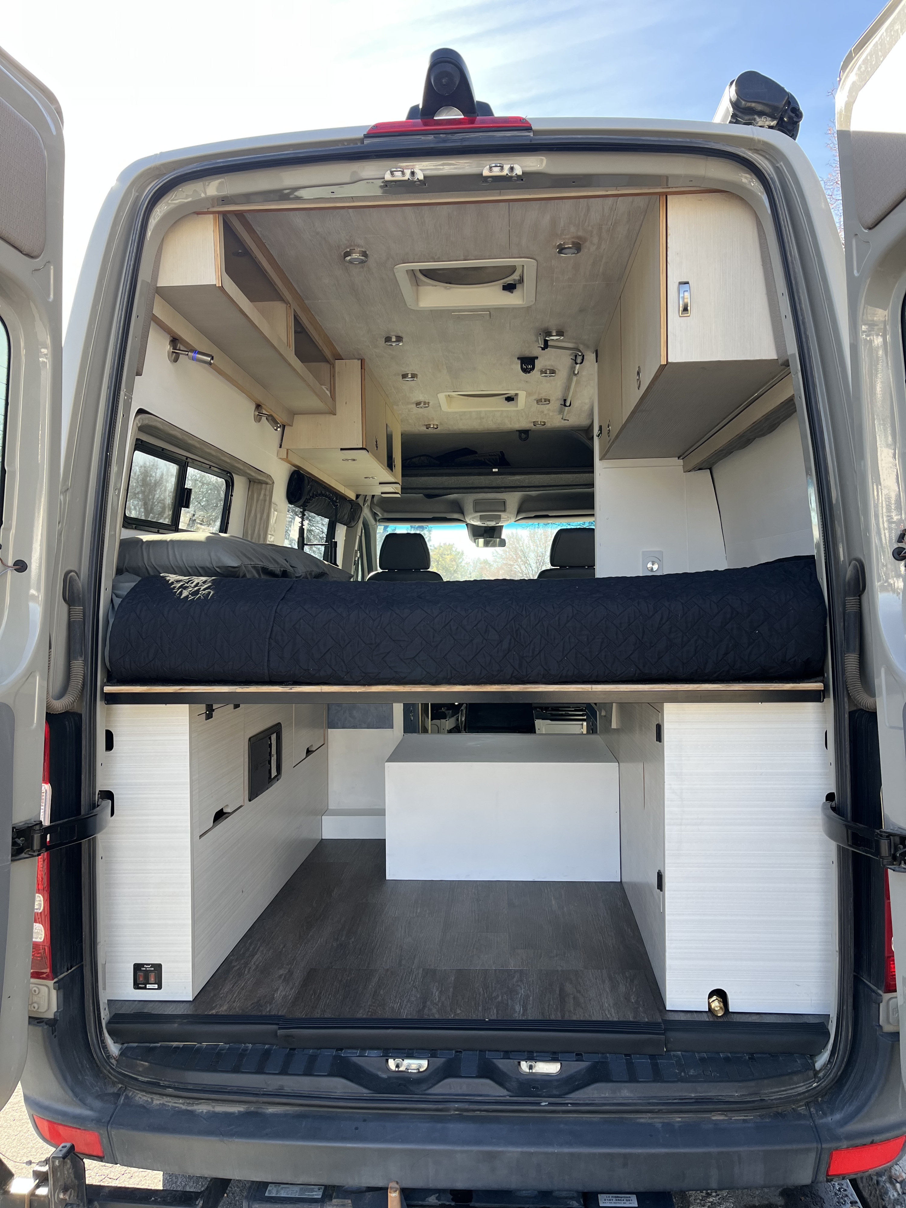 Modern camper van interior, showcasing a raised bed, storage units, and ceiling amenities. Perfect for an RV rental adventure.. Mercedes Sprinter 2017