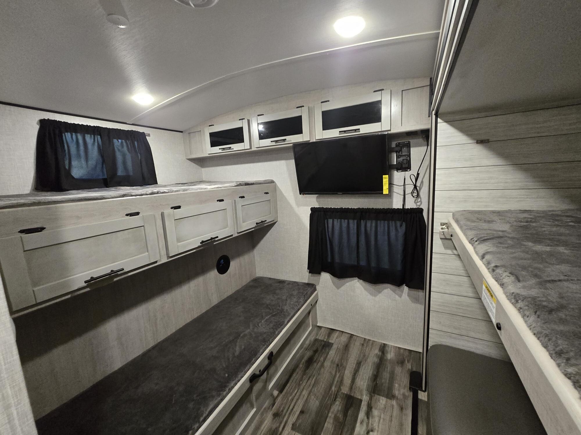 RV rental bunkhouse: light wood bunks, gray bedding, wall-mounted TV, and overhead storage. Ideal for camping.. Crossroads RV Sunset Trail 2023