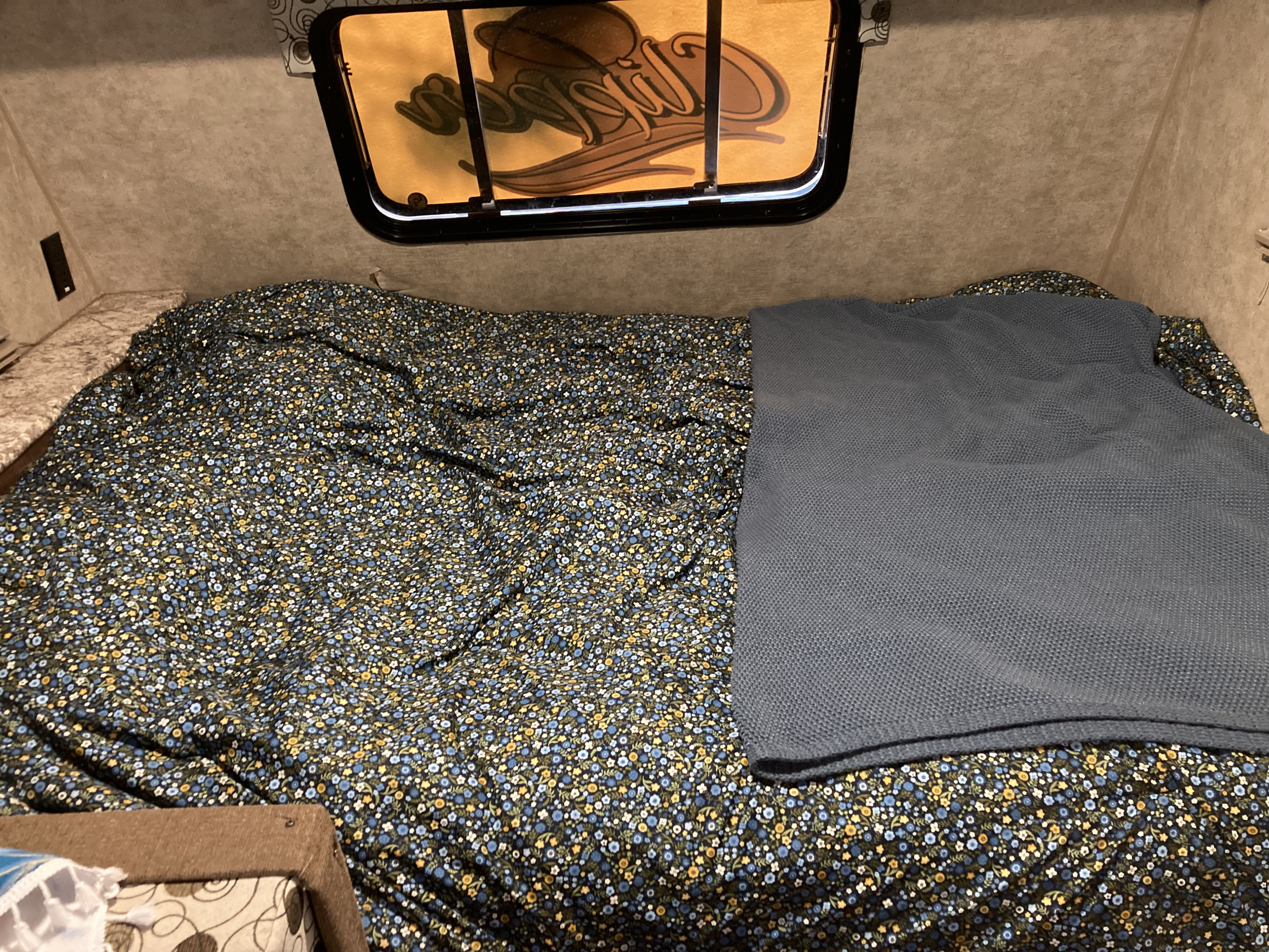 Cozy RV rental bed, featuring a dark floral patterned comforter and a folded grey knitted blanket, ready for your trip.. Clipper 17BH 2018