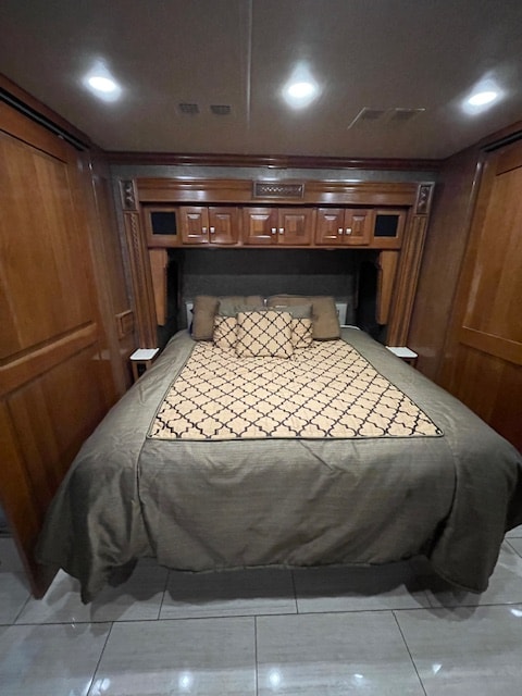 Cozy RV rental bedroom featuring a large bed with patterned bedding, surrounded by elegant wood cabinetry and recessed lighting.. Holiday Rambler Endeavor 2018