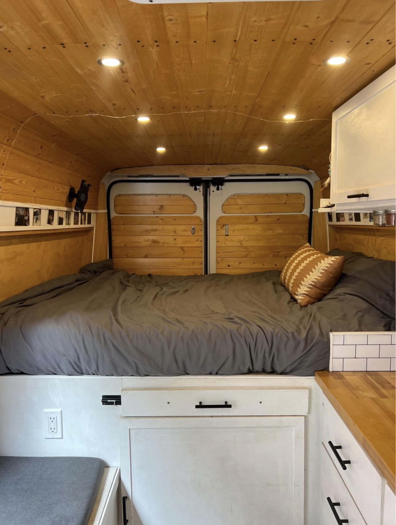 Cozy RV rental bedroom with a grey bed, patterned pillow, wooden walls/ceiling, and built-in storage.. Dodge Ram 2500 ProMaster 2015