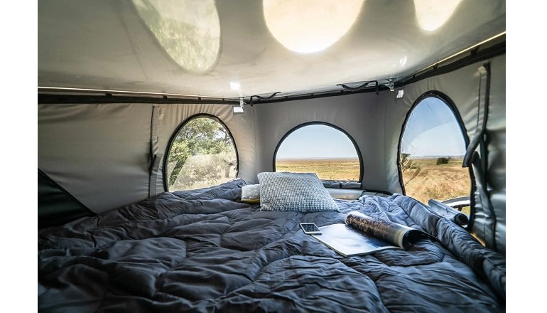 Cozy RV rental pop-up camper interior with comfy bed, smartphone, and scenic views through round windows for outdoor adventures.. Pilote CV500 2026