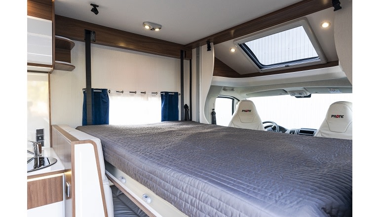 Interior of an RV rental featuring a comfortable bed, compact kitchenette, and a skylight above the driving cabin.. Pilote P726FGJ 2026