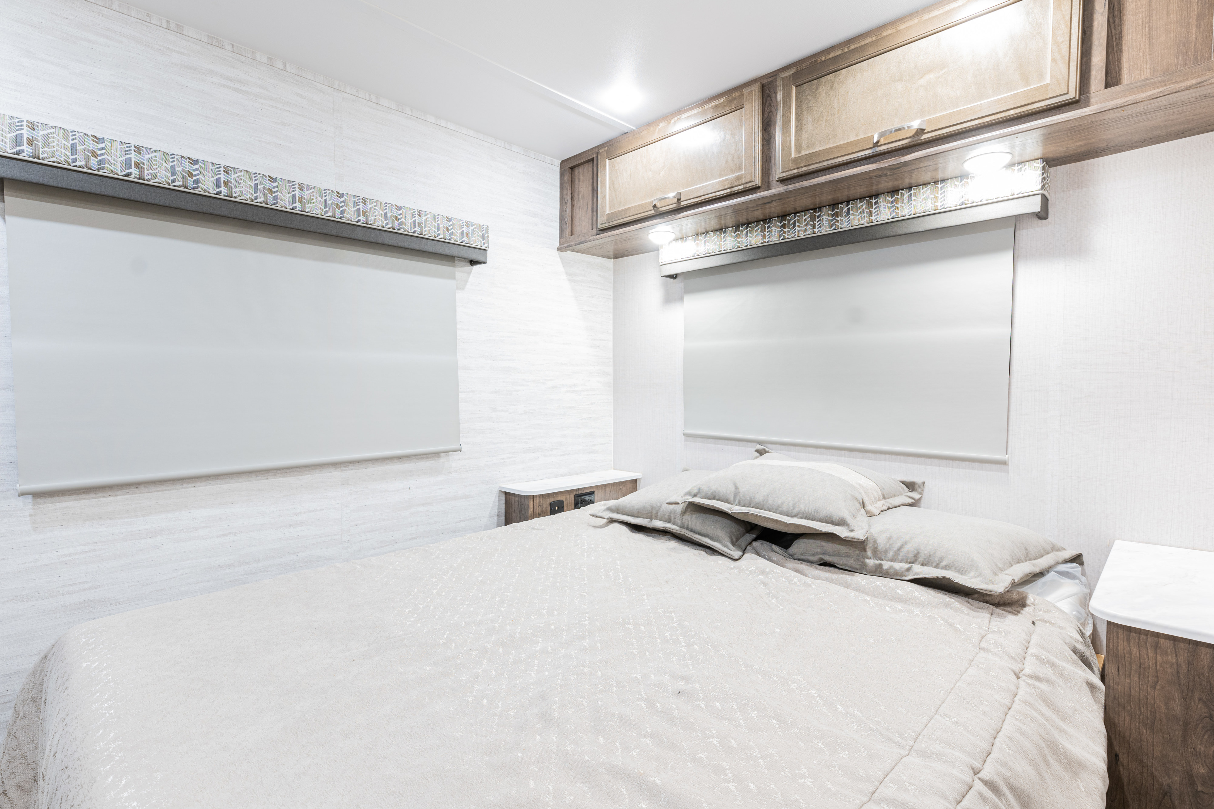 Modern RV rental bedroom with a comfortable bed, light walls, roller blinds, decorative valances, and wood overhead storage.. Gulf Stream Yellowstone 2023