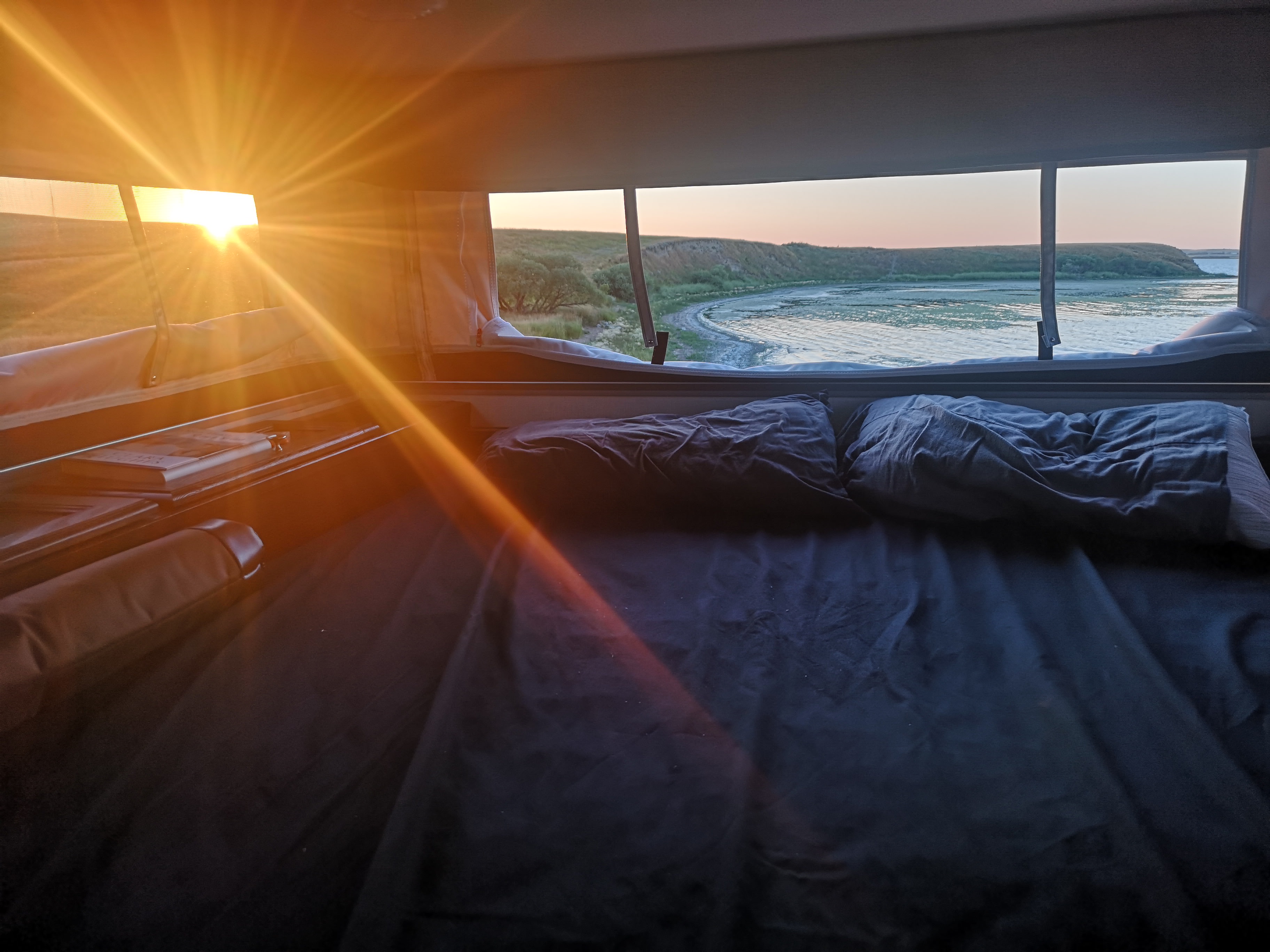 Waking up in your RV rental to a beautiful sunrise over a lake. Cozy bed, scenic view, perfect for camping adventurers.. Palomino Real-Lite 2018