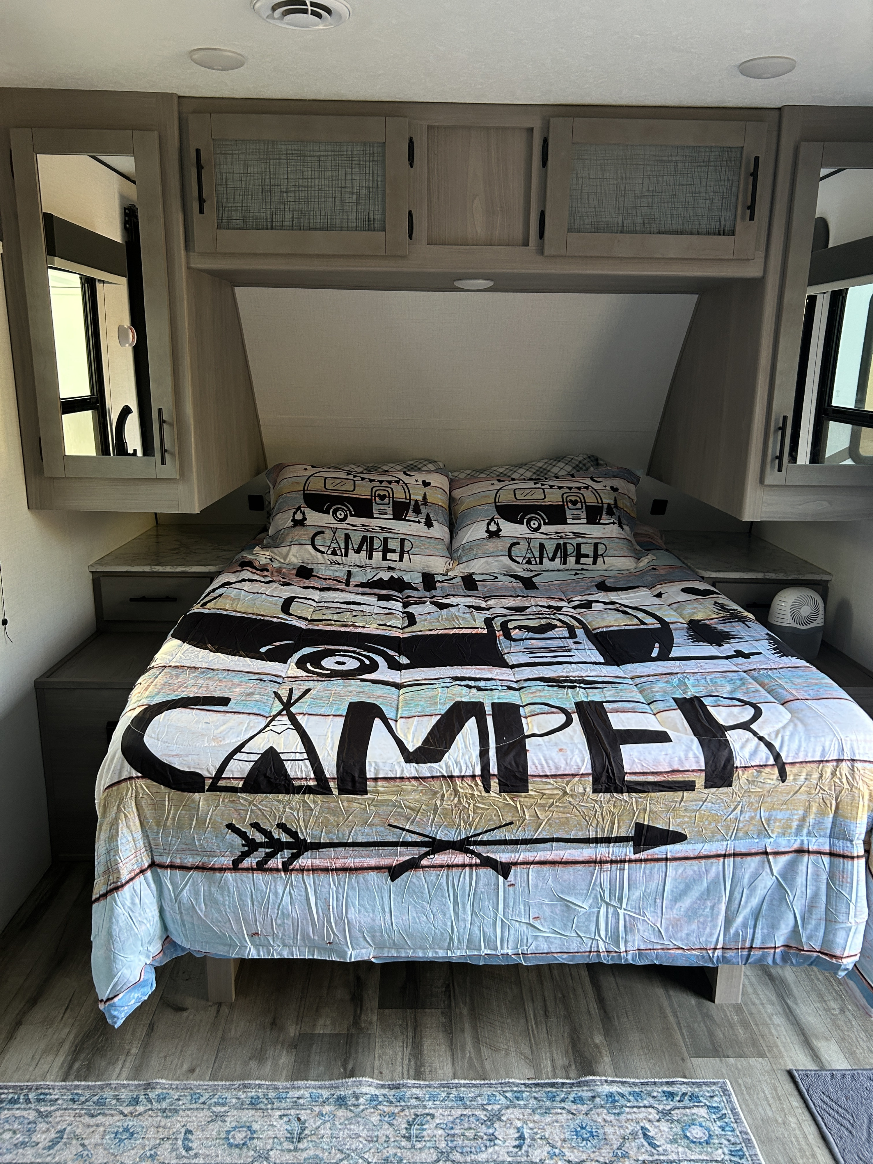 This cozy RV rental bedroom features a fun "CAMPER" themed bed, overhead storage, and side tables for a comfy trip.. Dutchmen Coleman Light 2024