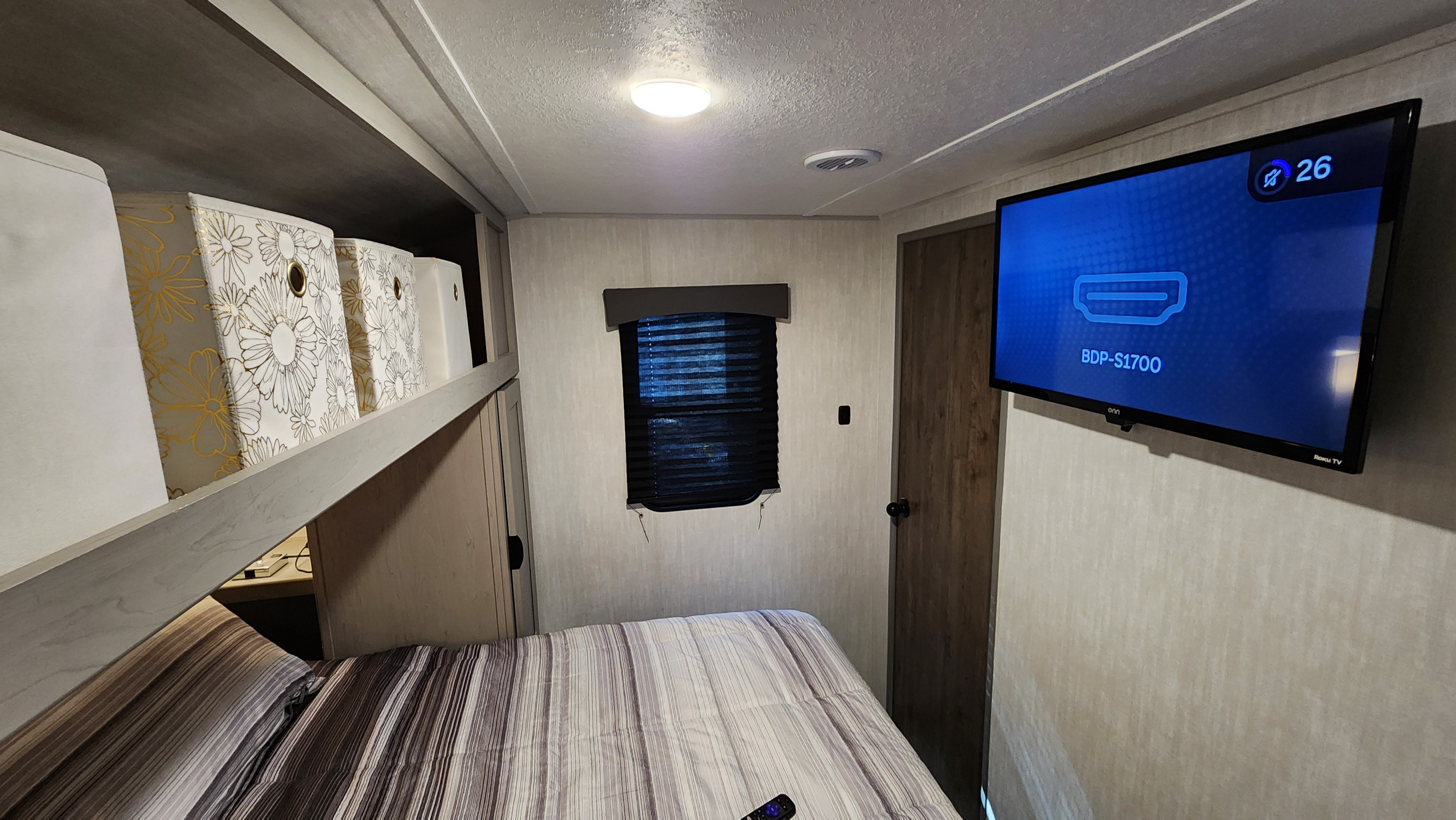 RV rental bedroom with TV (HDMI input), striped bedding, overhead storage, window, and bright ceiling lights.. Forest River Viking 6K 2025