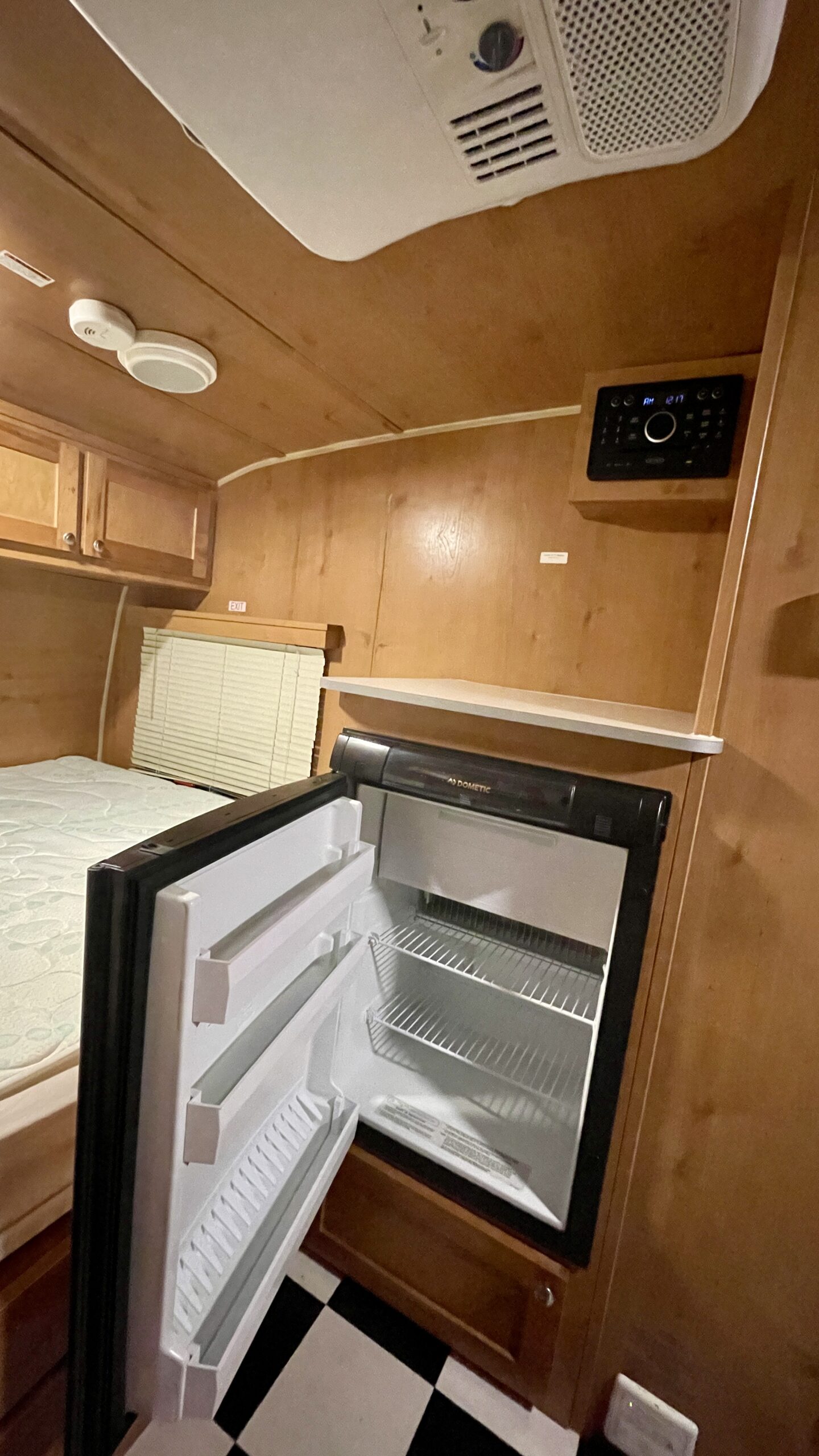 Inside this RV rental: wooden walls, an open mini-fridge, bed, AC unit, and stereo. A cozy, functional compact space.. Riverside Retro 2018