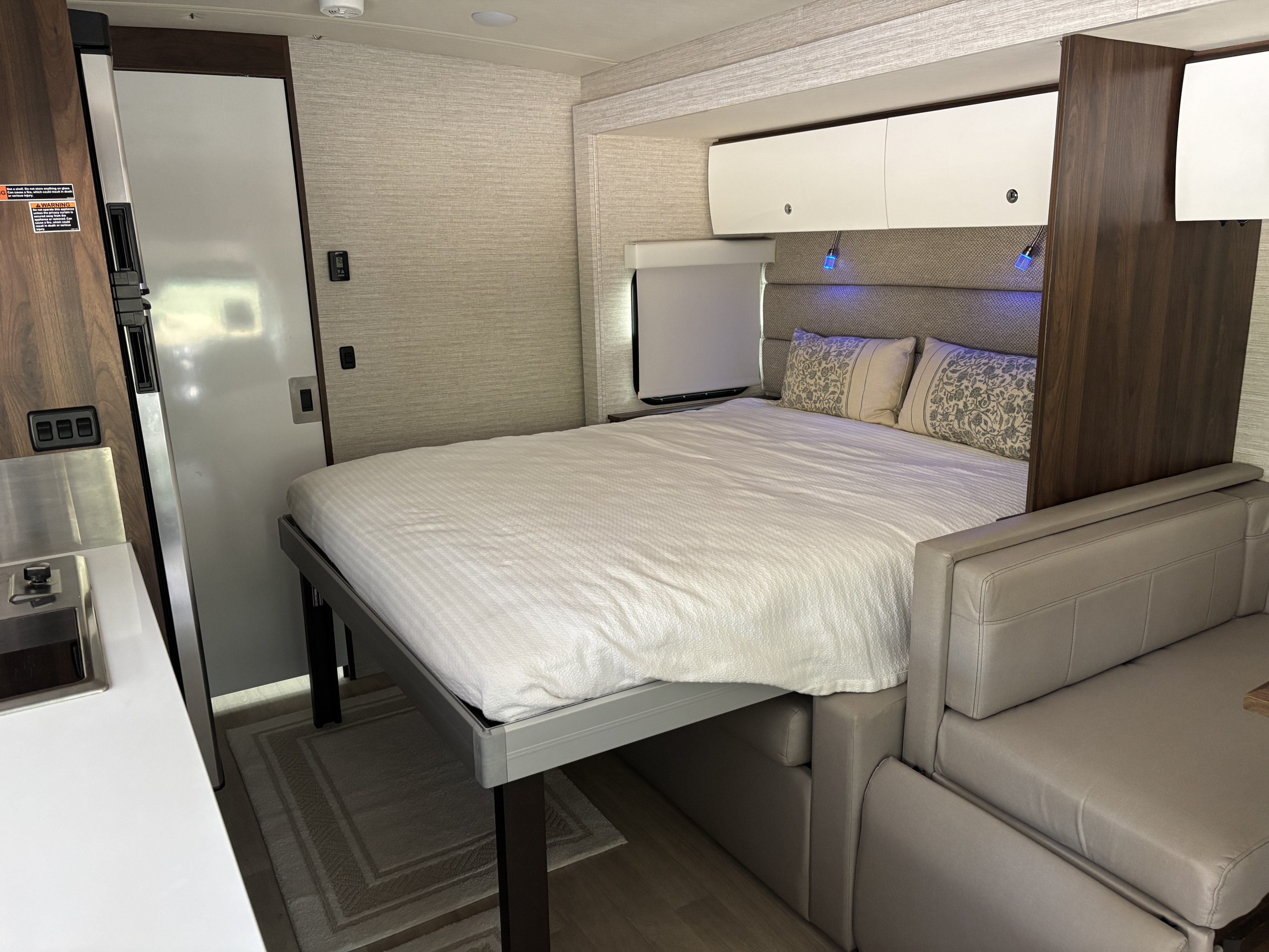 Cozy RV rental interior with a bed, overhead storage, sofa, and mini kitchen on the left.. Winnebago View 2021