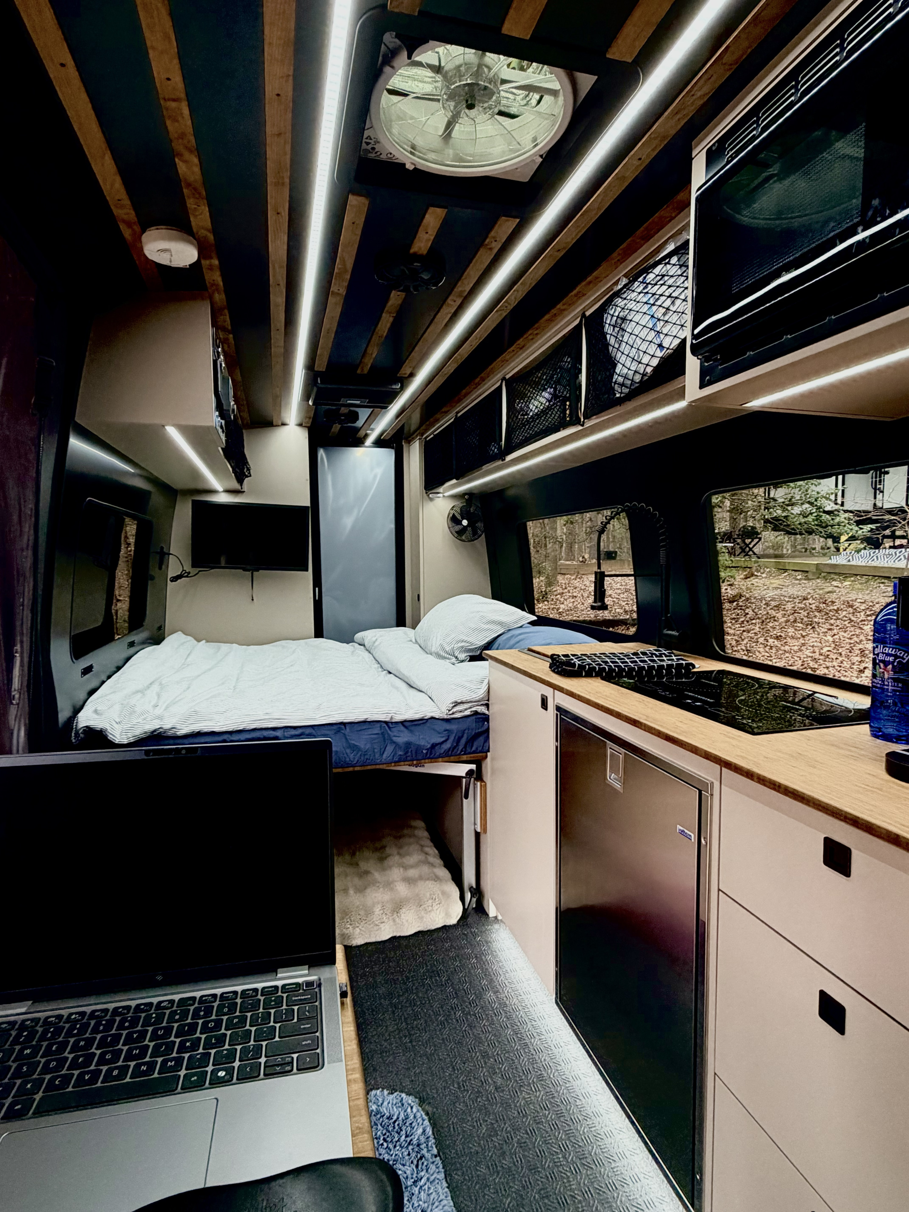 Cozy RV rental interior: laptop workspace, comfy bed, kitchenette with fridge & cooktop. Ideal for travel.. 27North Venture Van 2025
