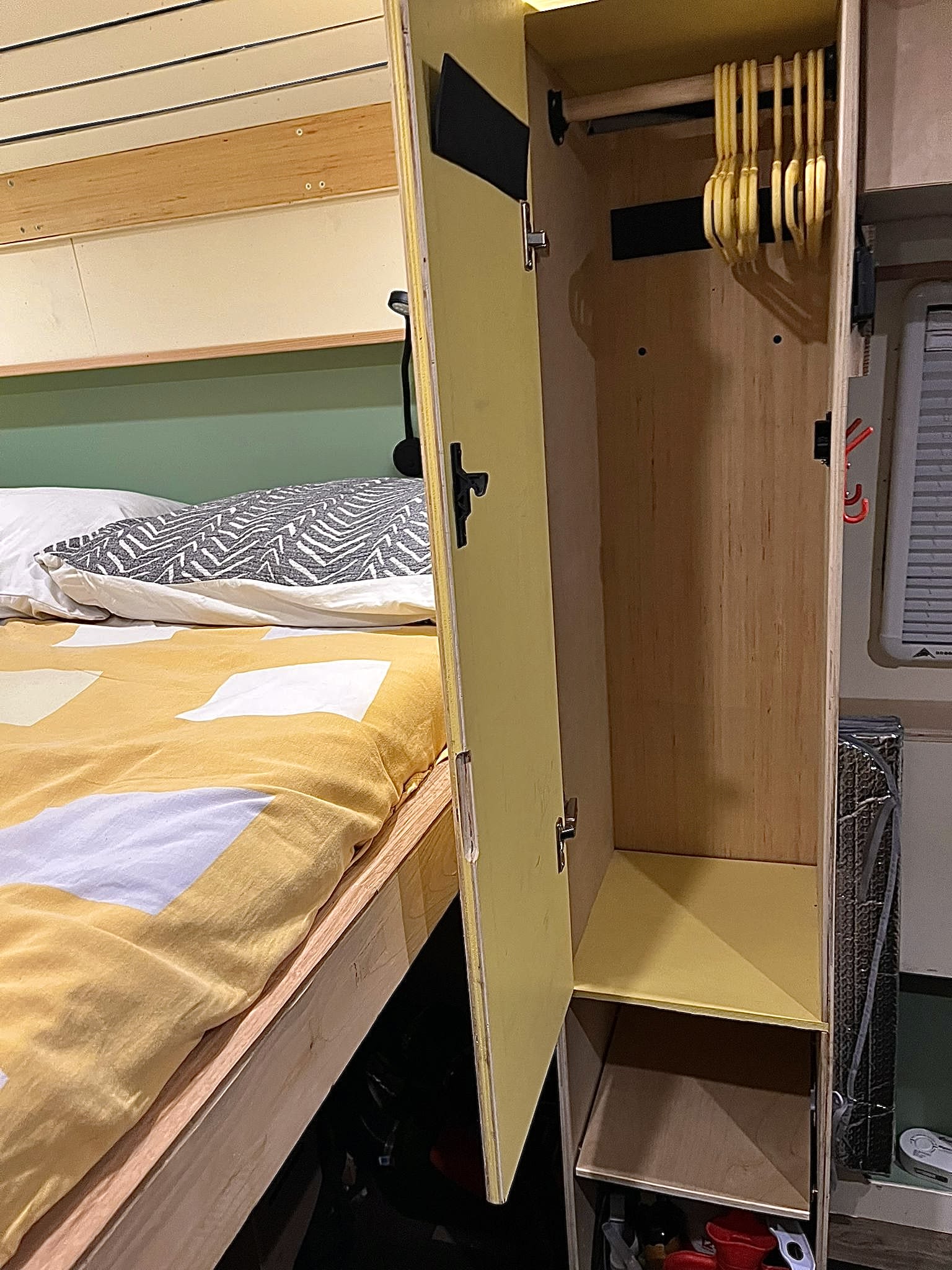 RV rental interior featuring a cozy bed and an open wardrobe with hangers and shelves for compact storage.. Ford Transit 2017