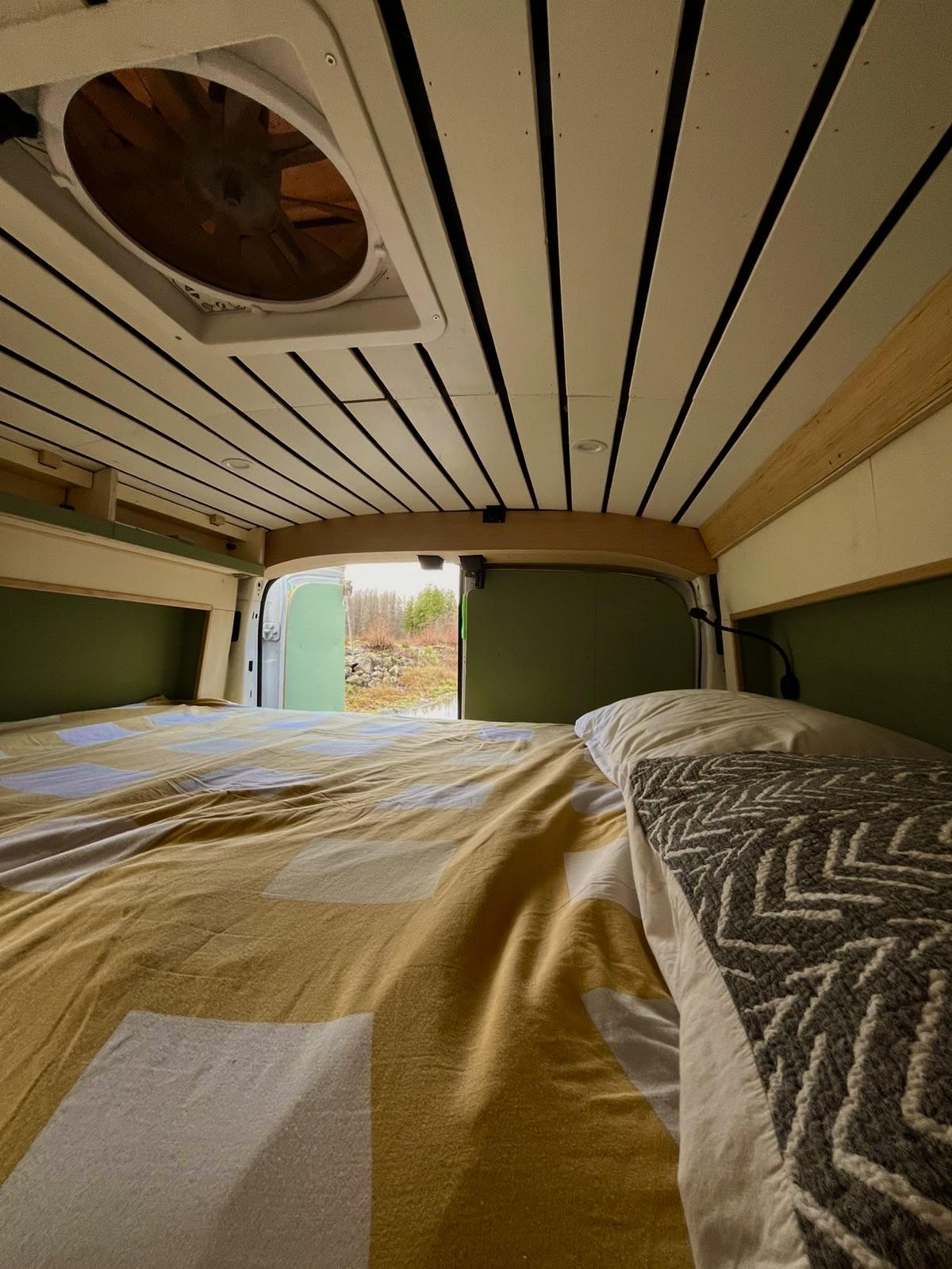Cozy camper van bed with a roof fan and open rear doors revealing nature, perfect for your next rv rental adventure!. Ford Transit 2017