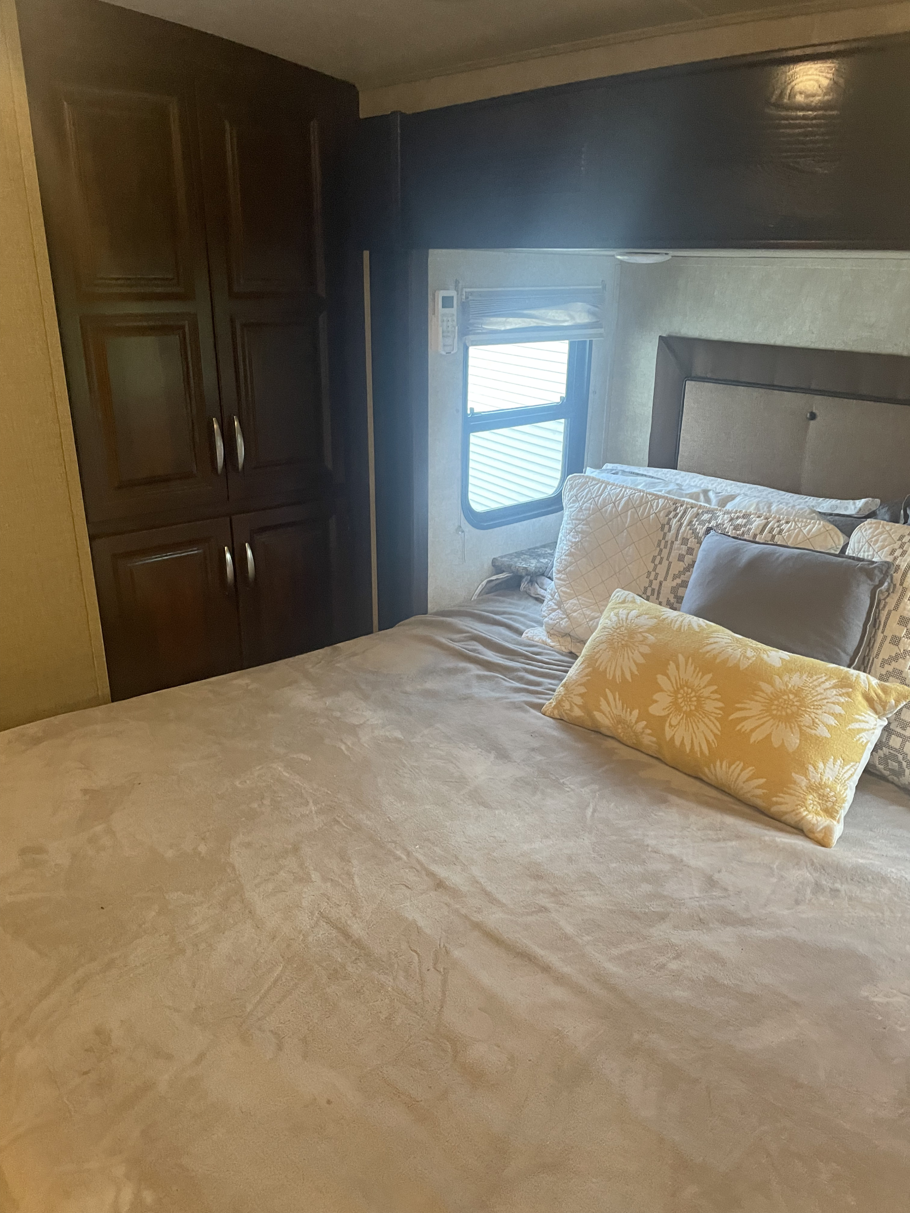 Cozy RV rental bedroom featuring a plush bed with decorative pillows, dark wood cabinets, and a window.. Keystone RV Montana Mountaineer 2015