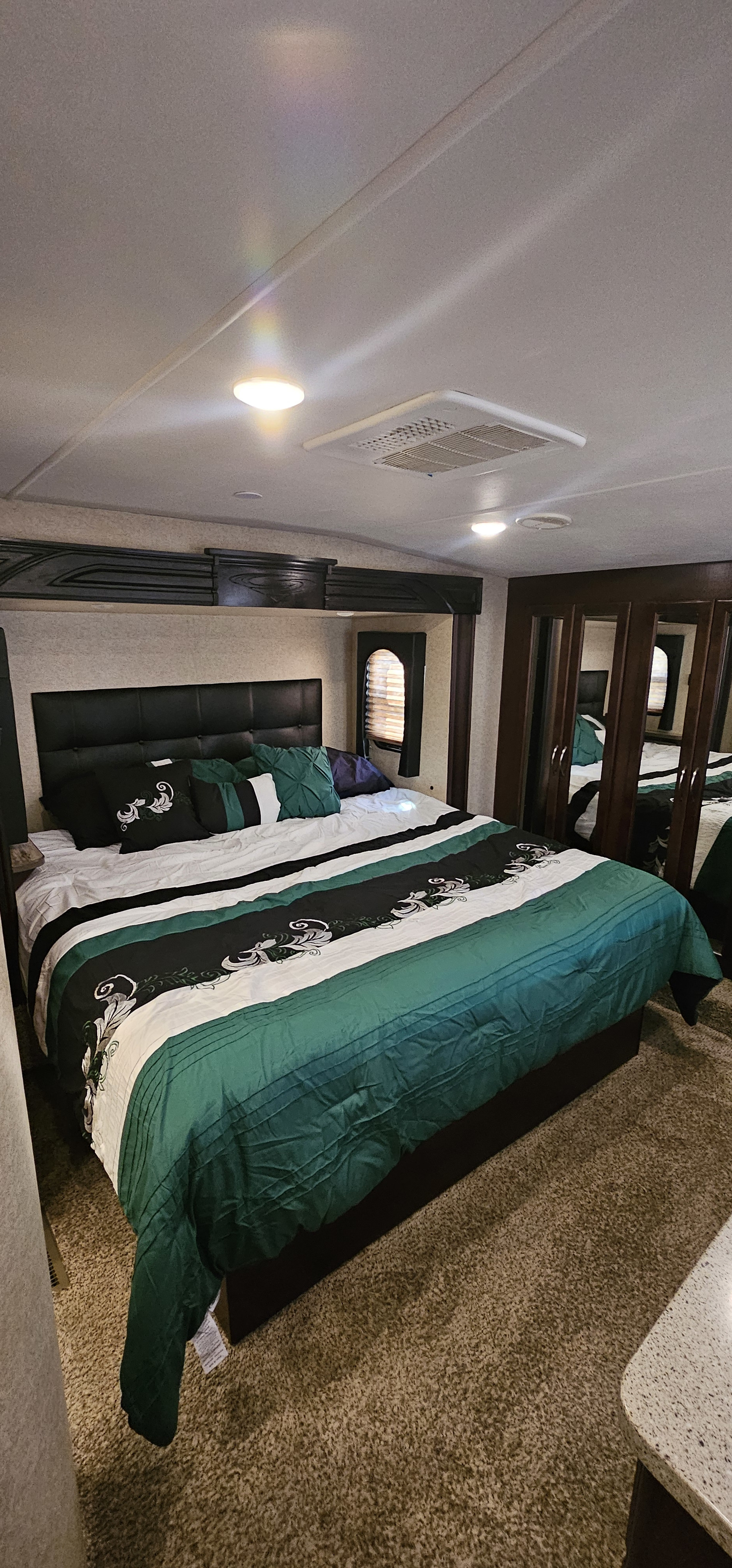 This RV rental features a well-appointed bedroom with a large bed, mirrored wardrobe, and overhead AC, offering a comfortable space on the road.. Heartland Cyclone 2015