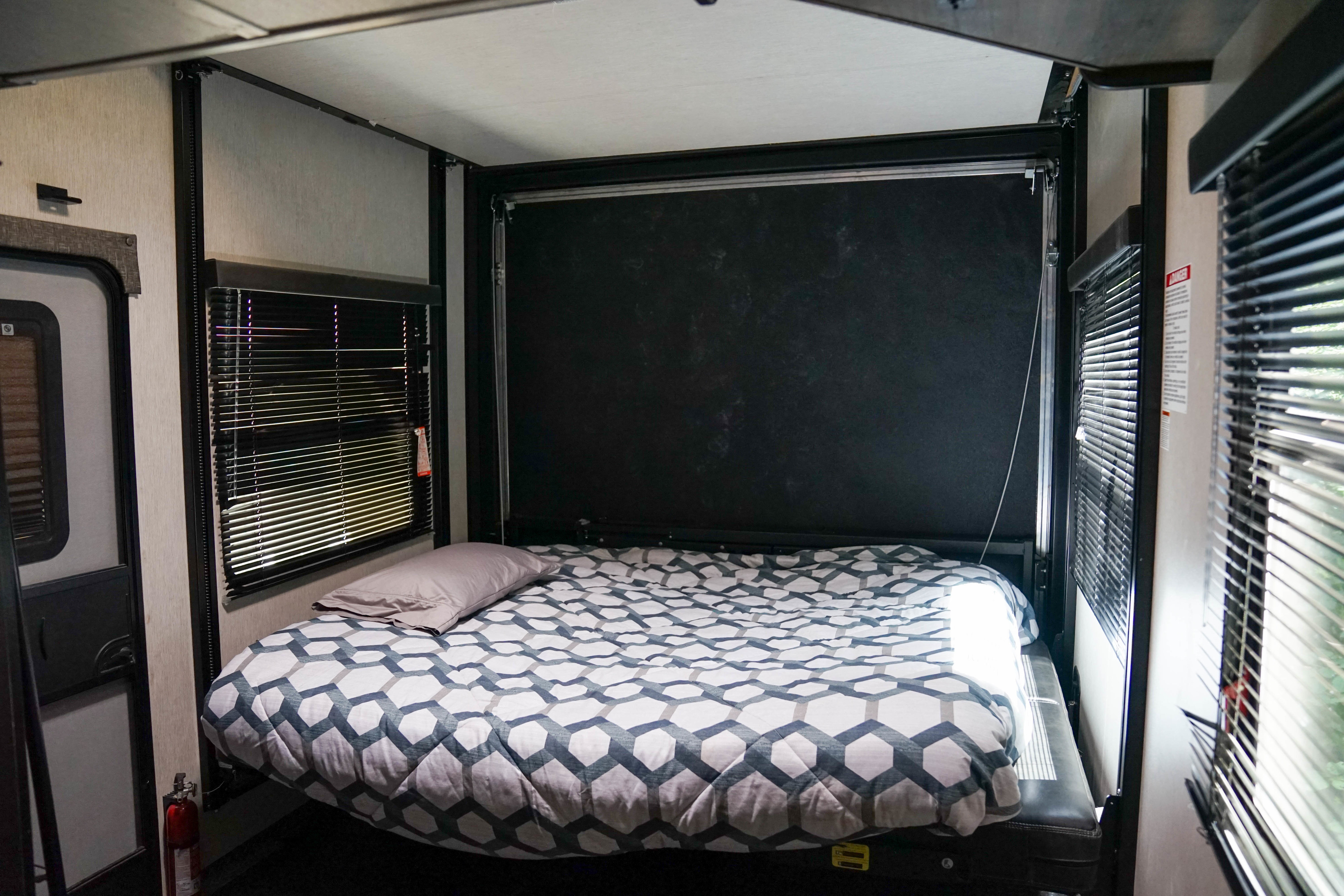 RV rental interior featuring a cozy bed with geometric bedding, windows with blinds, and a fire extinguisher.. Heartland RVs Torque Toy Hauler 2019