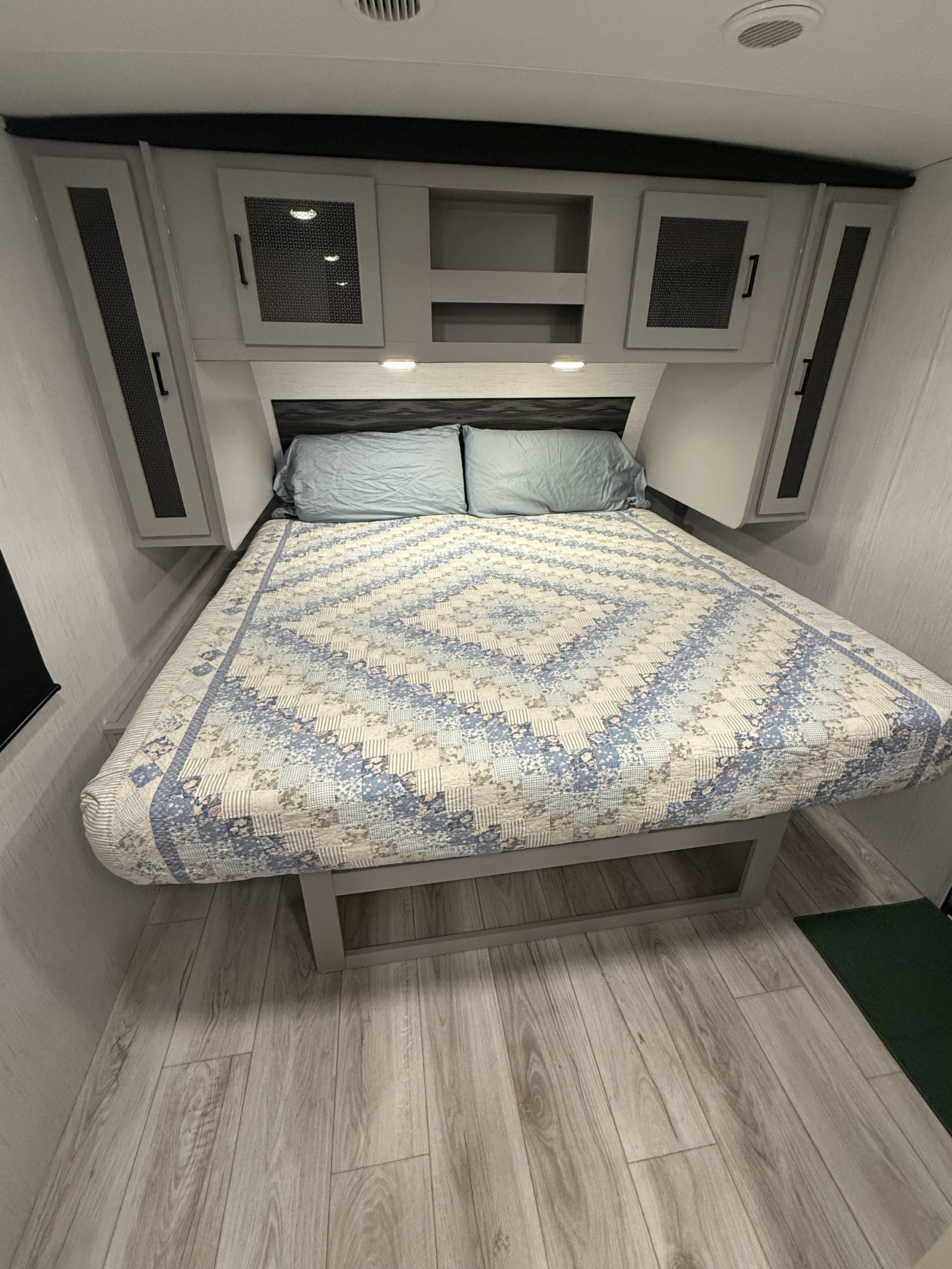 Cozy RV bedroom with light wood floors, overhead cabinets, and a patterned quilt, ideal for an RV rental.. Heartland RVs North Trail 2023