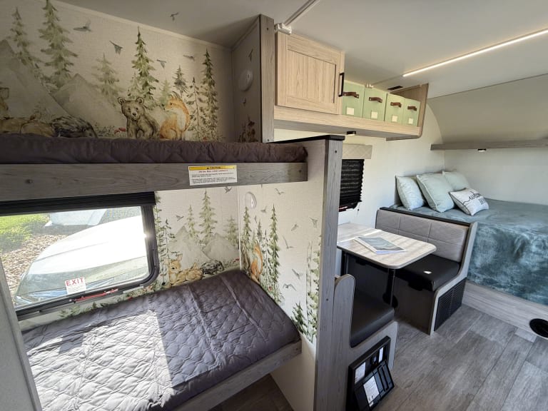 Family-friendly RV rental interior with forest-themed bunk beds, dinette, and main bed. Perfect for adventure.. Heartland RVs Mallard 2025