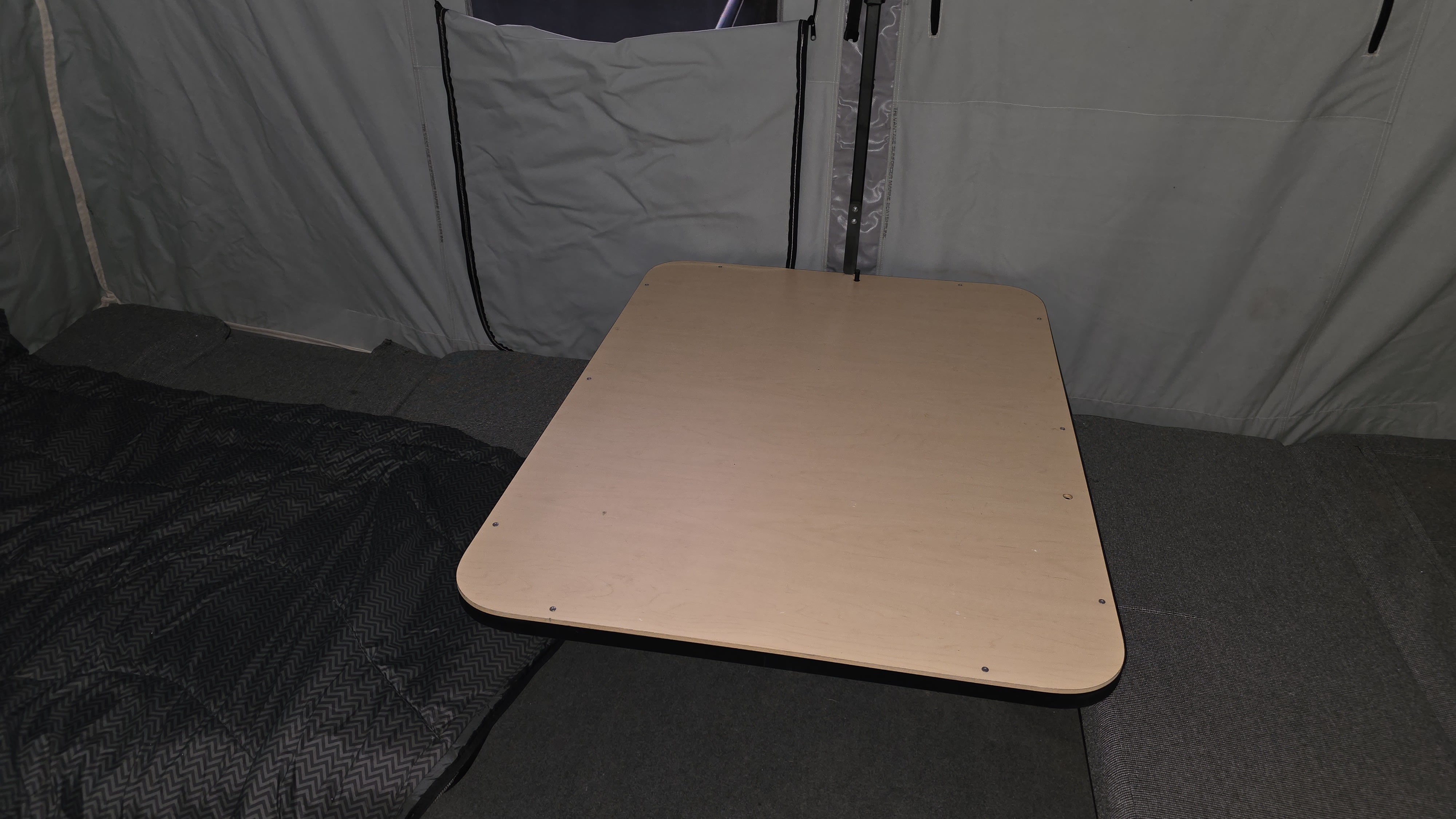 Interior of an RV rental: a light wood table and sleeping area within a pop-up camper's grey fabric walls.. Jumping Jack 6x8 ft 2012