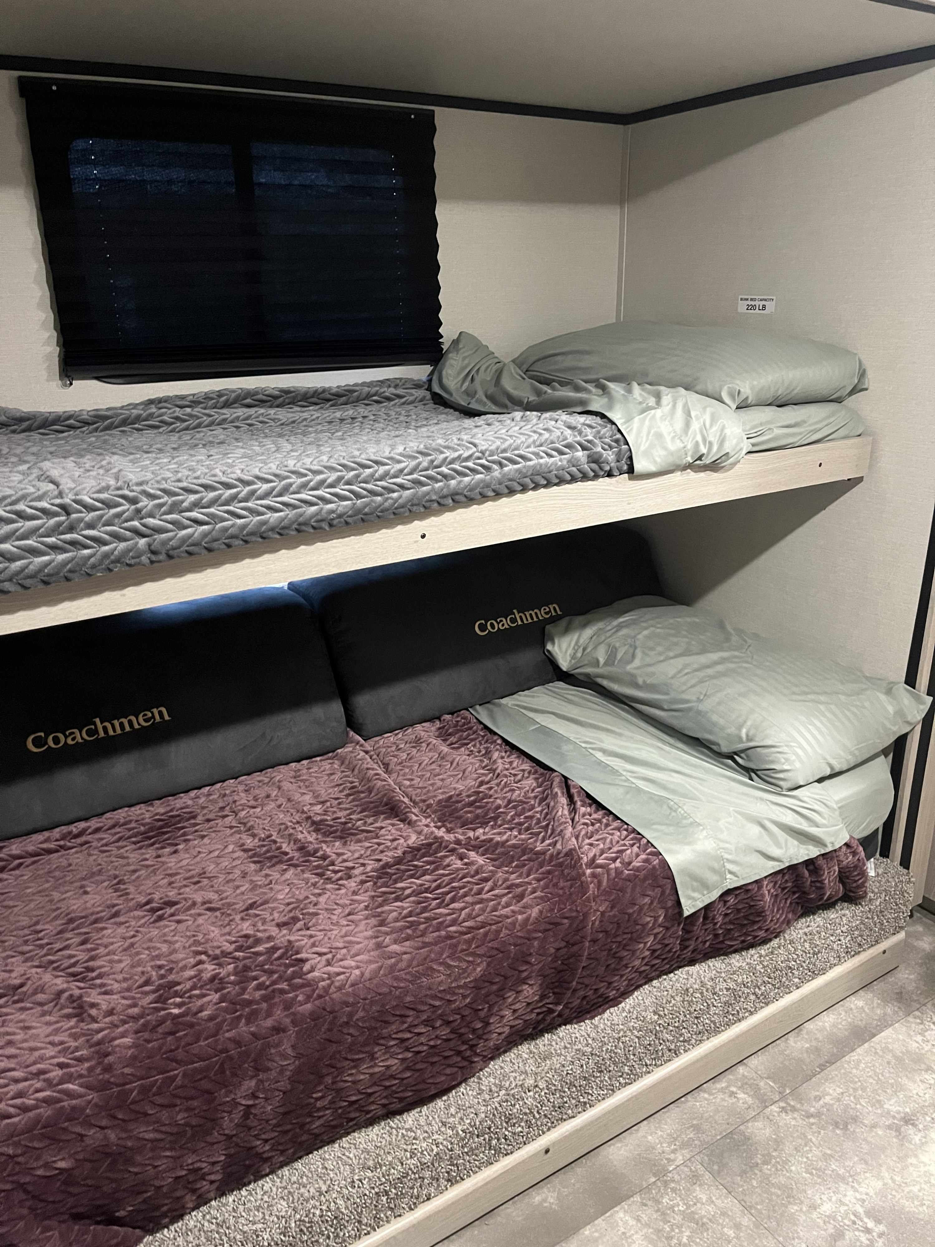 RV rental bunk beds: a cozy interior view with Coachmen branding, window, and a 220 LB capacity warning.. Coachmen Apex 2023