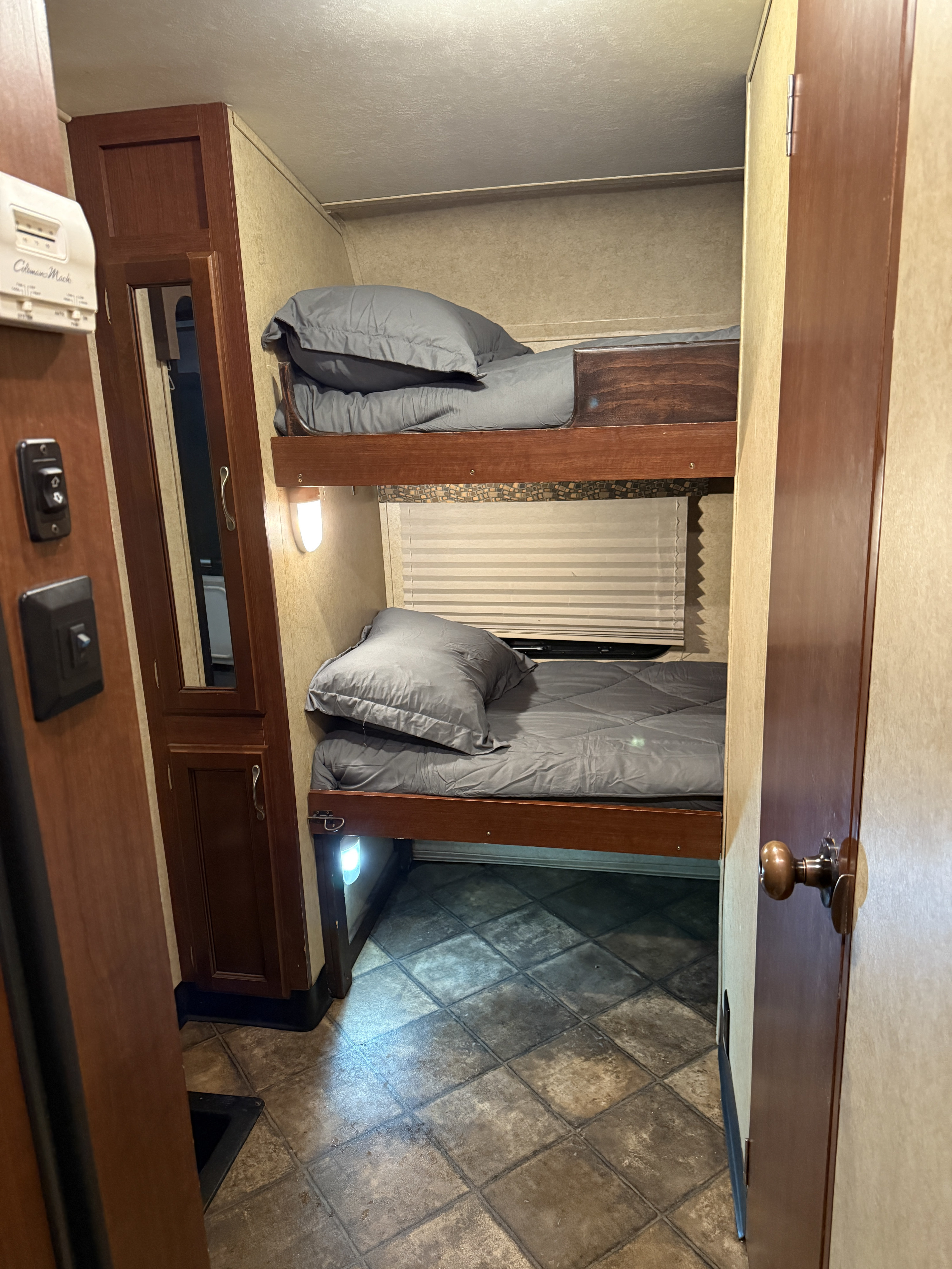 Compact sleeping area in an RV rental with stacked bunk beds, a thermostat, and small storage cabinet.. Evergreen RV Ascend 2015