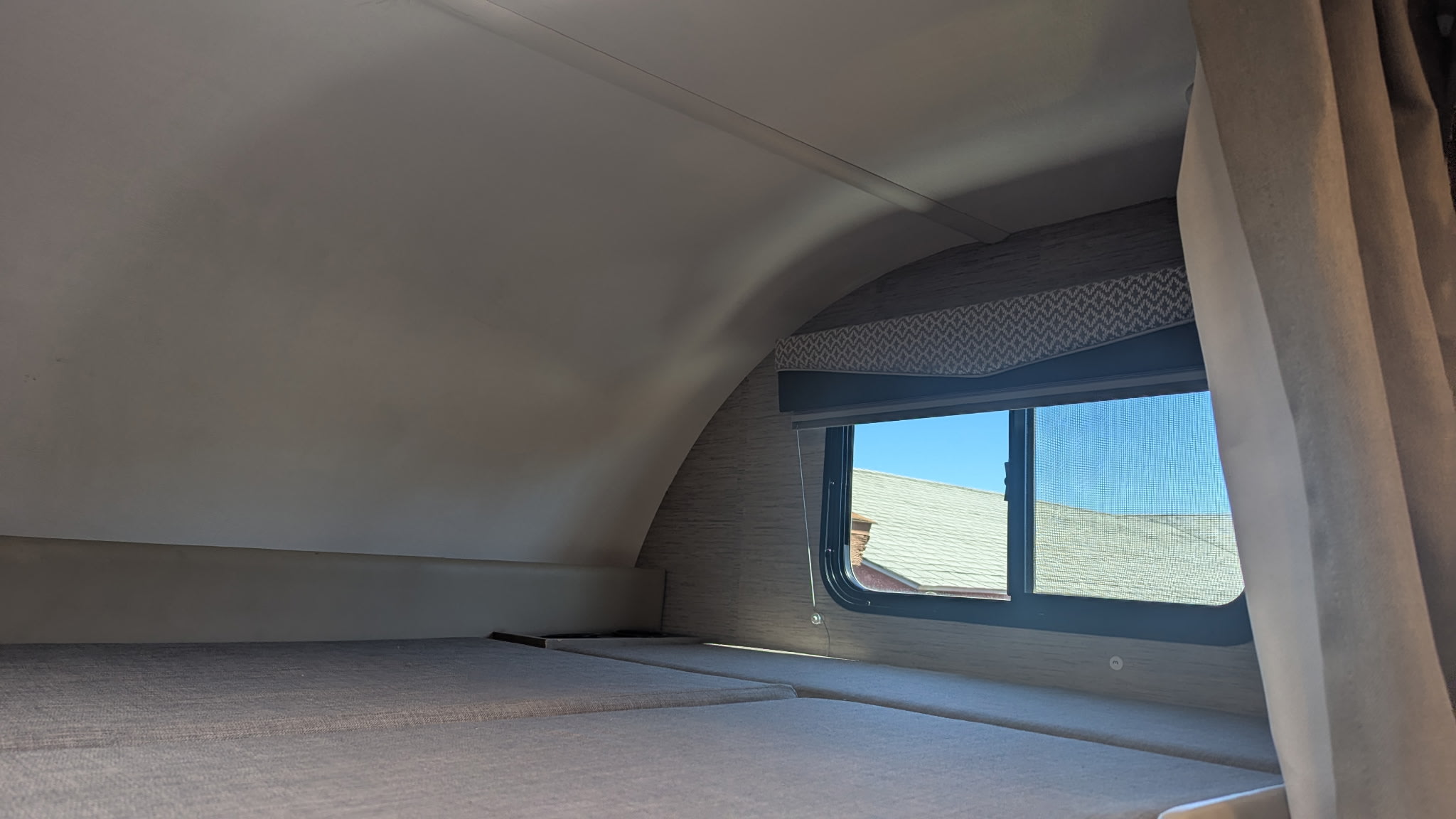 RV rental overhead bunk area. Features include a curved ceiling, a window, and a privacy curtain, ideal for camper sleeping.. Thor Four Winds 2022