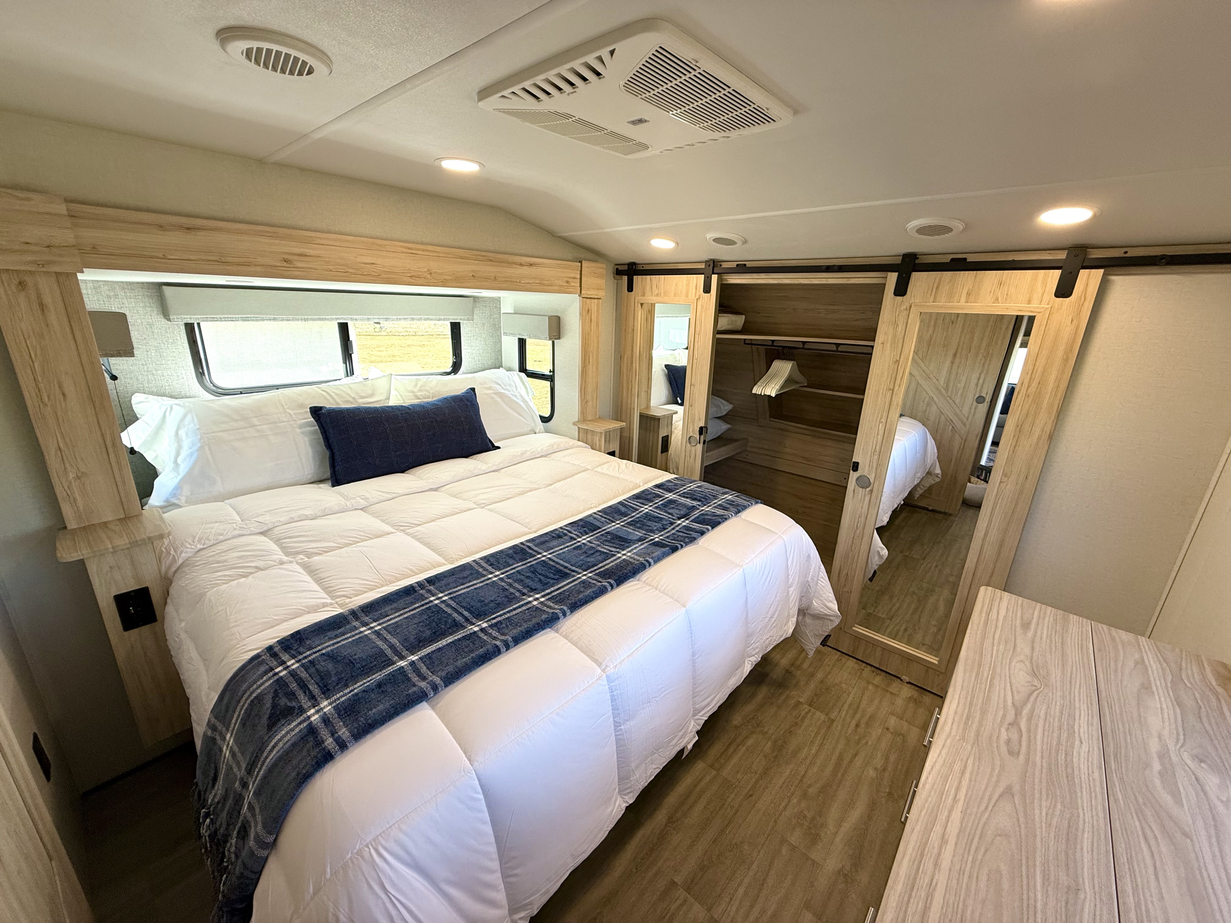 Cozy and modern RV rental bedroom featuring a comfortable bed, windows, and a barn door wardrobe for ample storage.. Alliance RV Avenue 2023