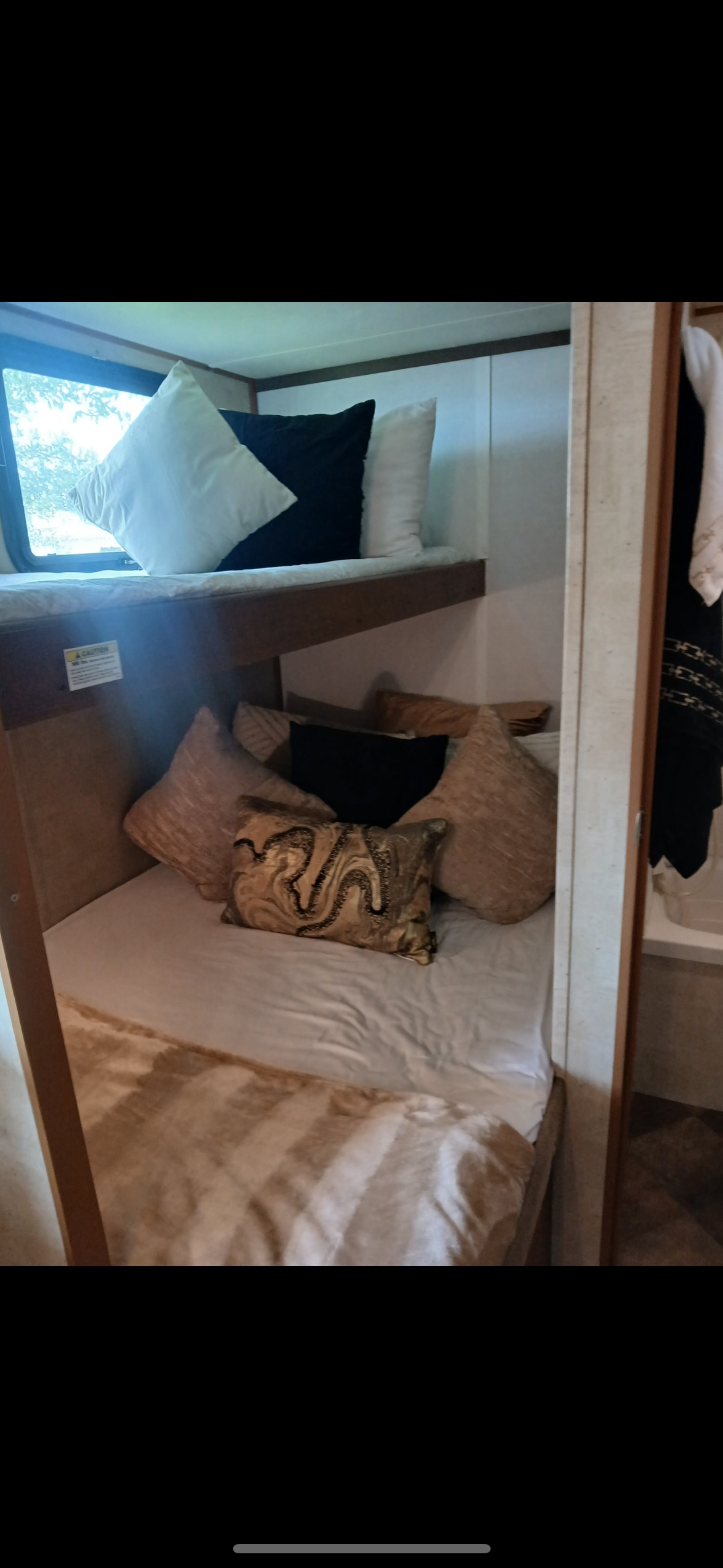 RV rental bunk beds: Two levels, with white and black pillows on the upper bunk by a window, and patterned pillows on the lower bunk.. Keystone RV Fireside 2014