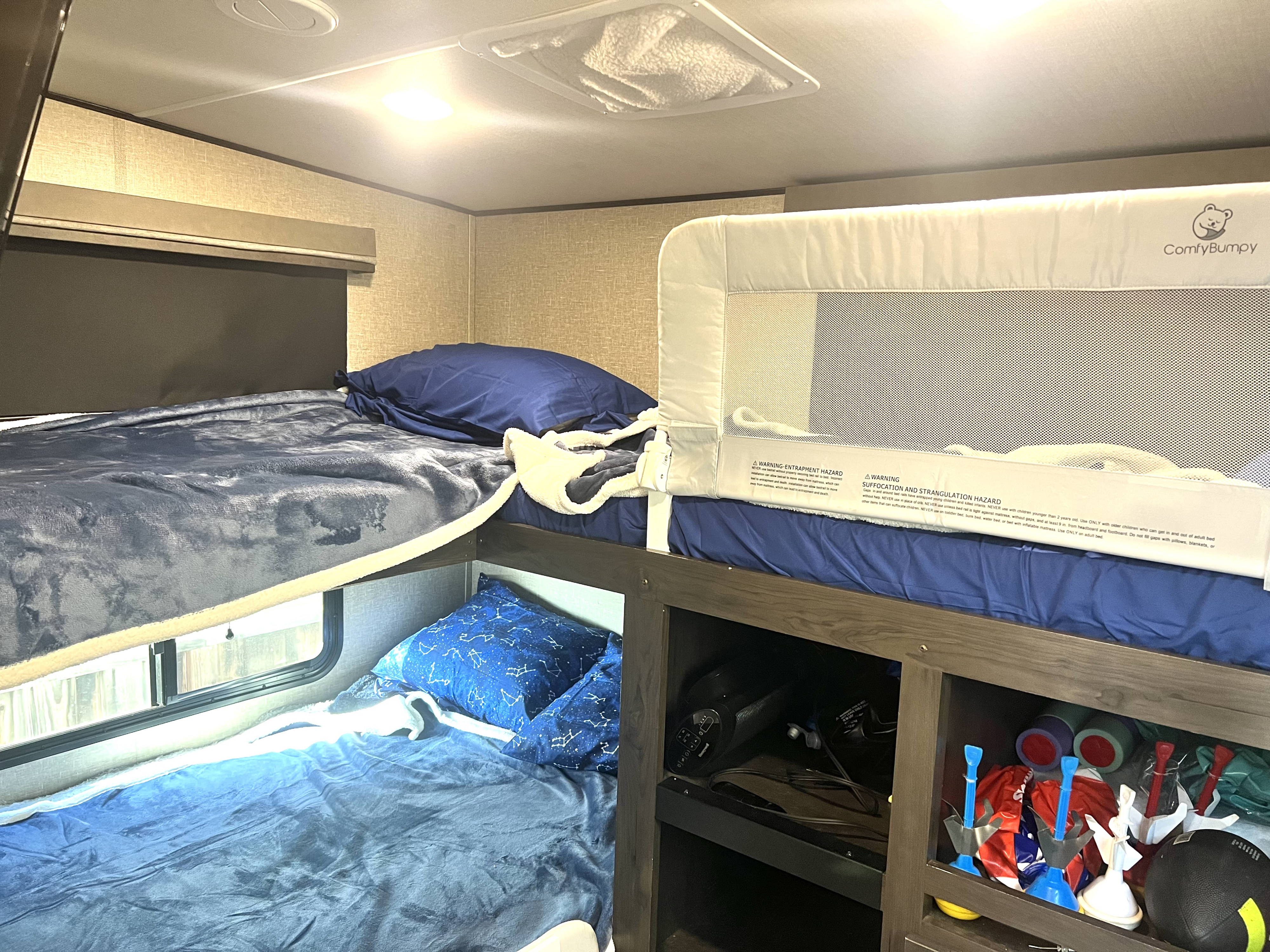 An RV rental's cozy bunk beds for children, featuring a "ComfyBumpy" safety rail on the top bunk and storage below.. Grand Design Reflection 2021