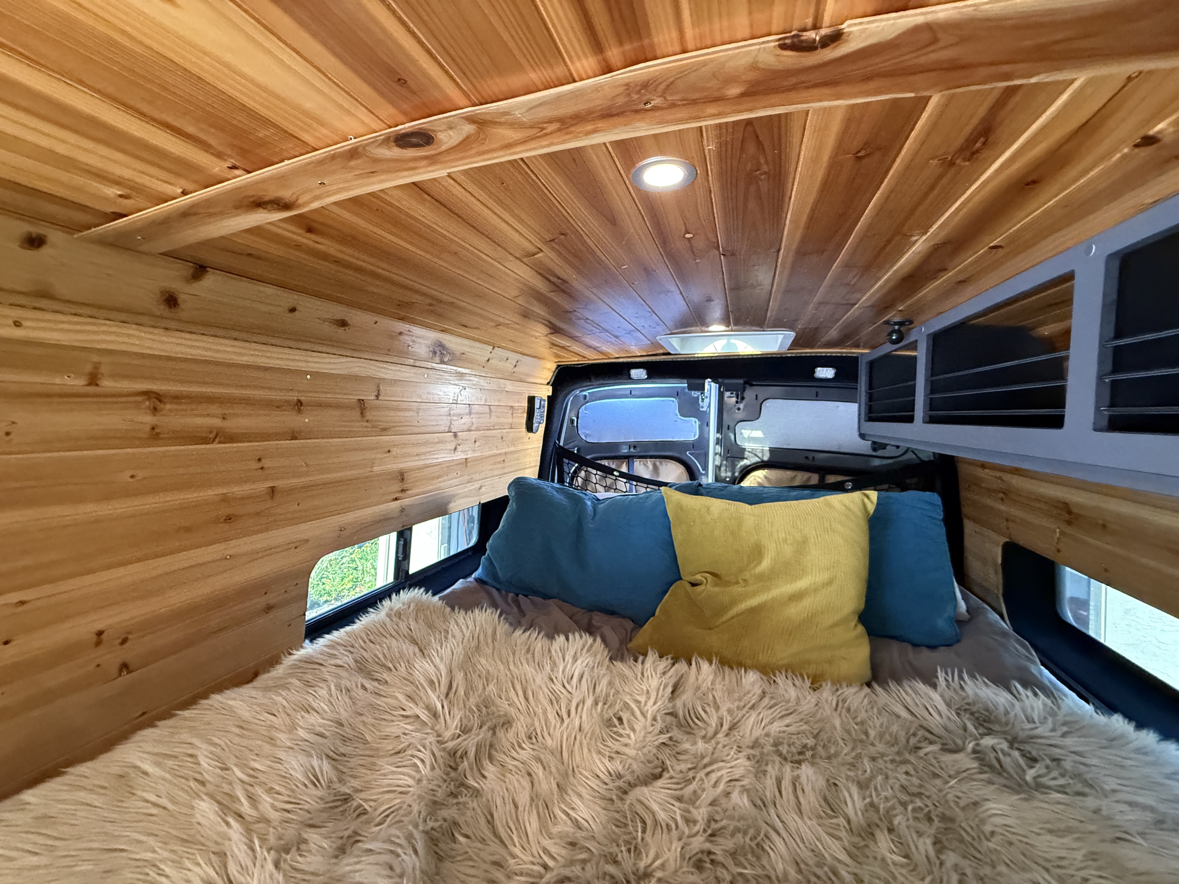 This cozy RV rental features a warm wooden camper van interior, complete with a comfortable bed and vibrant pillows.. Ford Transit Extended High-Roof 2018
