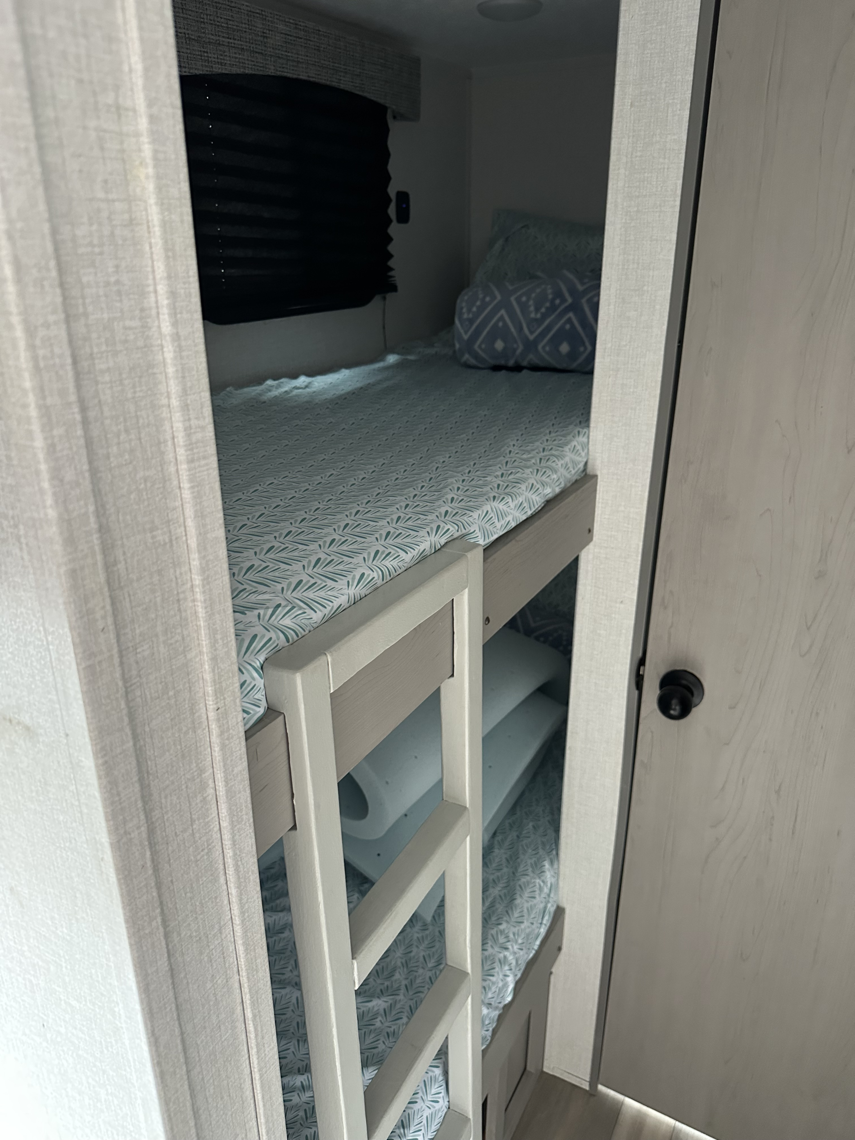 Compact bunk beds inside an RV rental, featuring patterned bedding and a ladder. Ideal, cozy sleeping area for travel.. Clipper 3K 2023