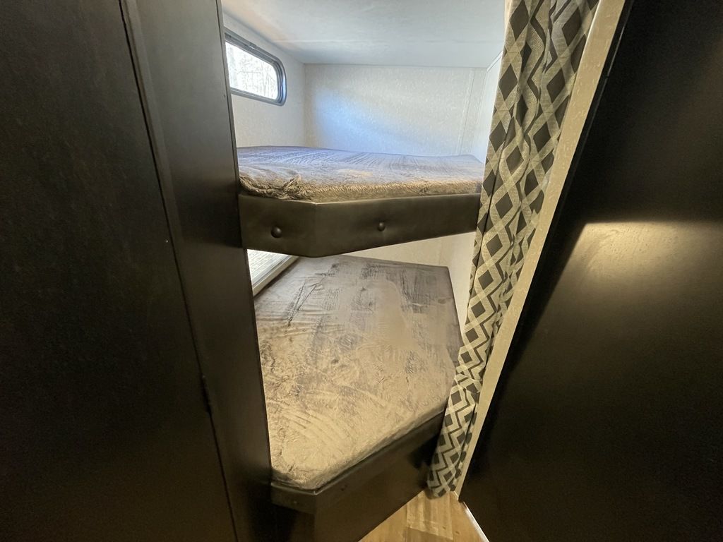 RV rental bunk beds: A view inside the sleeping area with dark frames, mattresses, a window, and patterned curtain.. Forest River Cherokee Grey Wolf Special Edition 2022