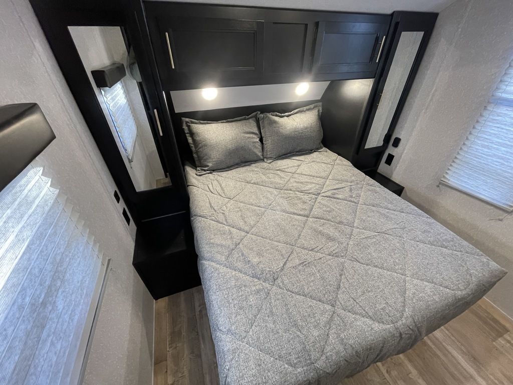 RV rental bedroom featuring a comfy bed with gray bedding, overhead cabinets, and mirrored side storage.. Forest River Cherokee Grey Wolf Special Edition 2022